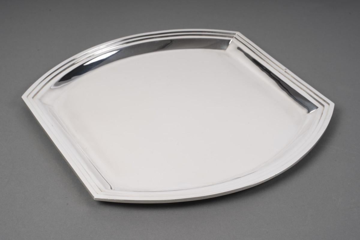 Plat carré en argent massif avec deux côtés latéraux incurvés

Dimensions : plateau : 30 X 30,5 cm, hauteur 1,5 cm

MATERIAL : Argent 1er titre 950/°°°

Poids : grammes

Cachet : MINERVE

Période : ART DECO circa 1930

Orfèvres : RAVINET