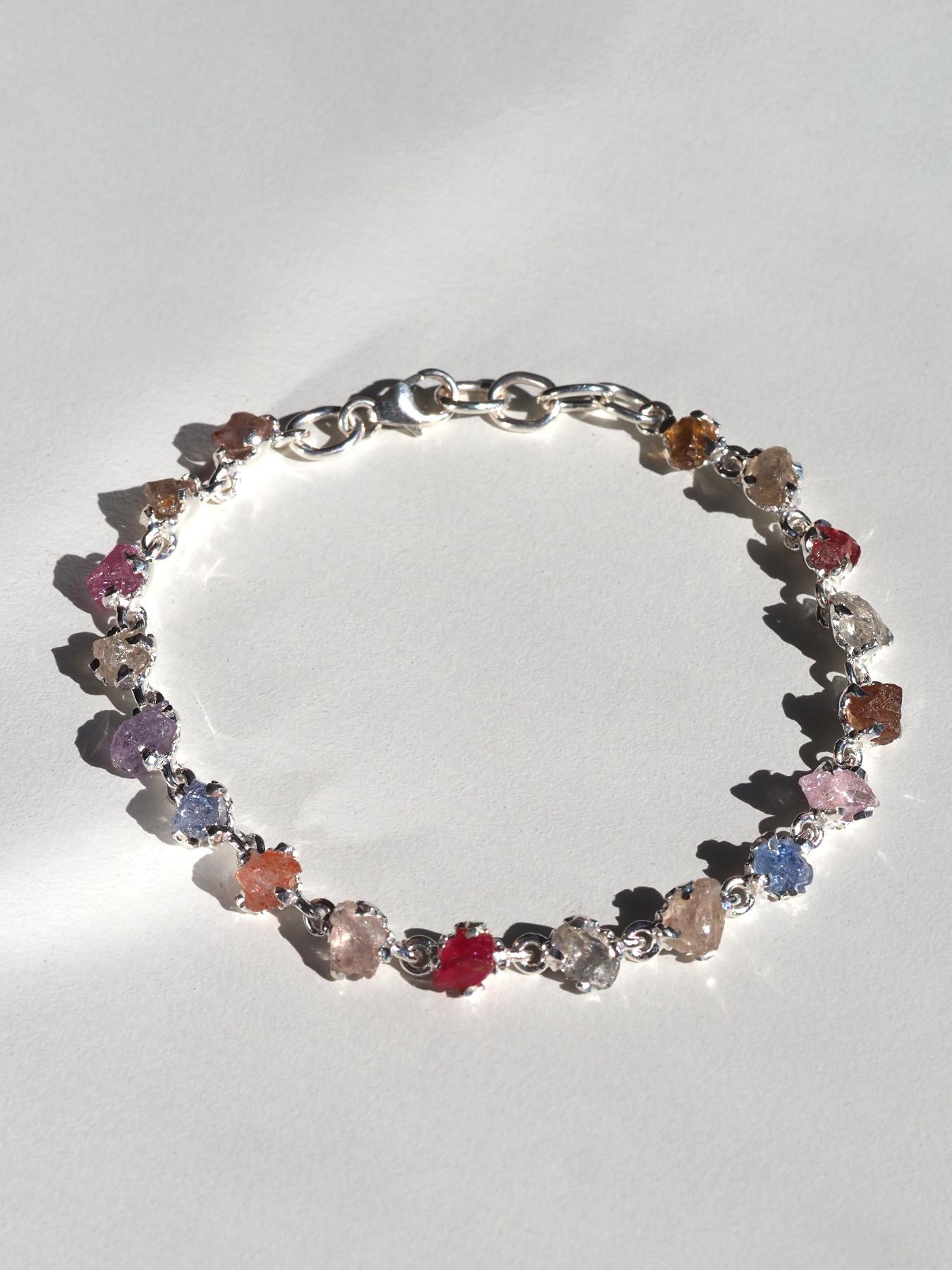 Un bracelet raffiné en argent sterling présentant 18 saphirs bruts naturels non traités dans un spectre de rose, jaune, rouge, ambre, bleu et violet. Chaque saphir provient du Sri Lanka et conserve sa forme cristalline brute et irrégulière, mesurant