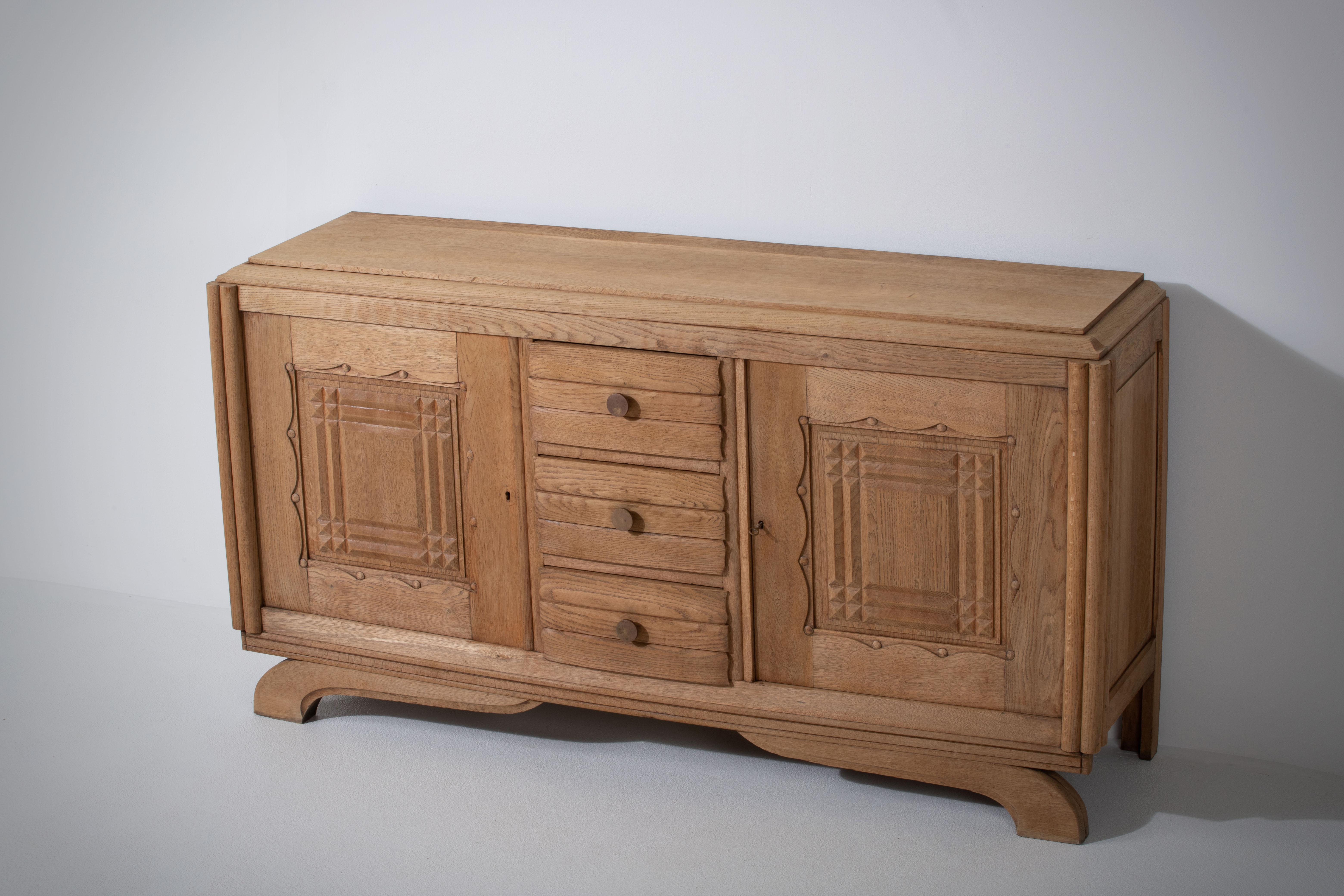 Credenza, solid oak, France, 1940s.
Art Deco Brutalist sideboard. 
The credenza consists of two storage facilities and covered with very detailed designed doors and in the center, a drawers column.
 
