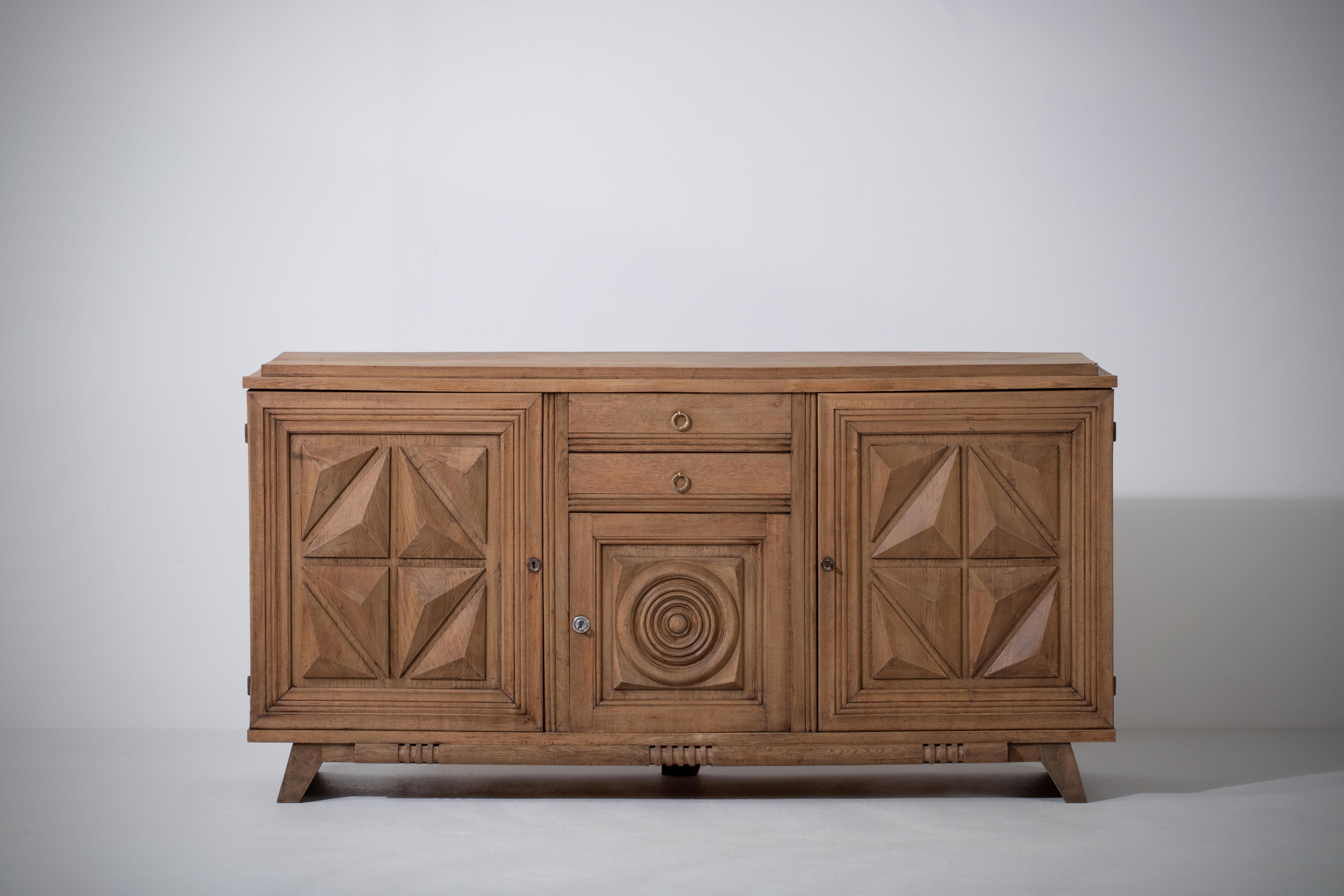 Credenza, solid oak, France, 1940s.
Art Deco Brutalist sideboard. 
The credenza consists of three storage facilities and covered with very detailed designed doors and in the center, a drawers column.