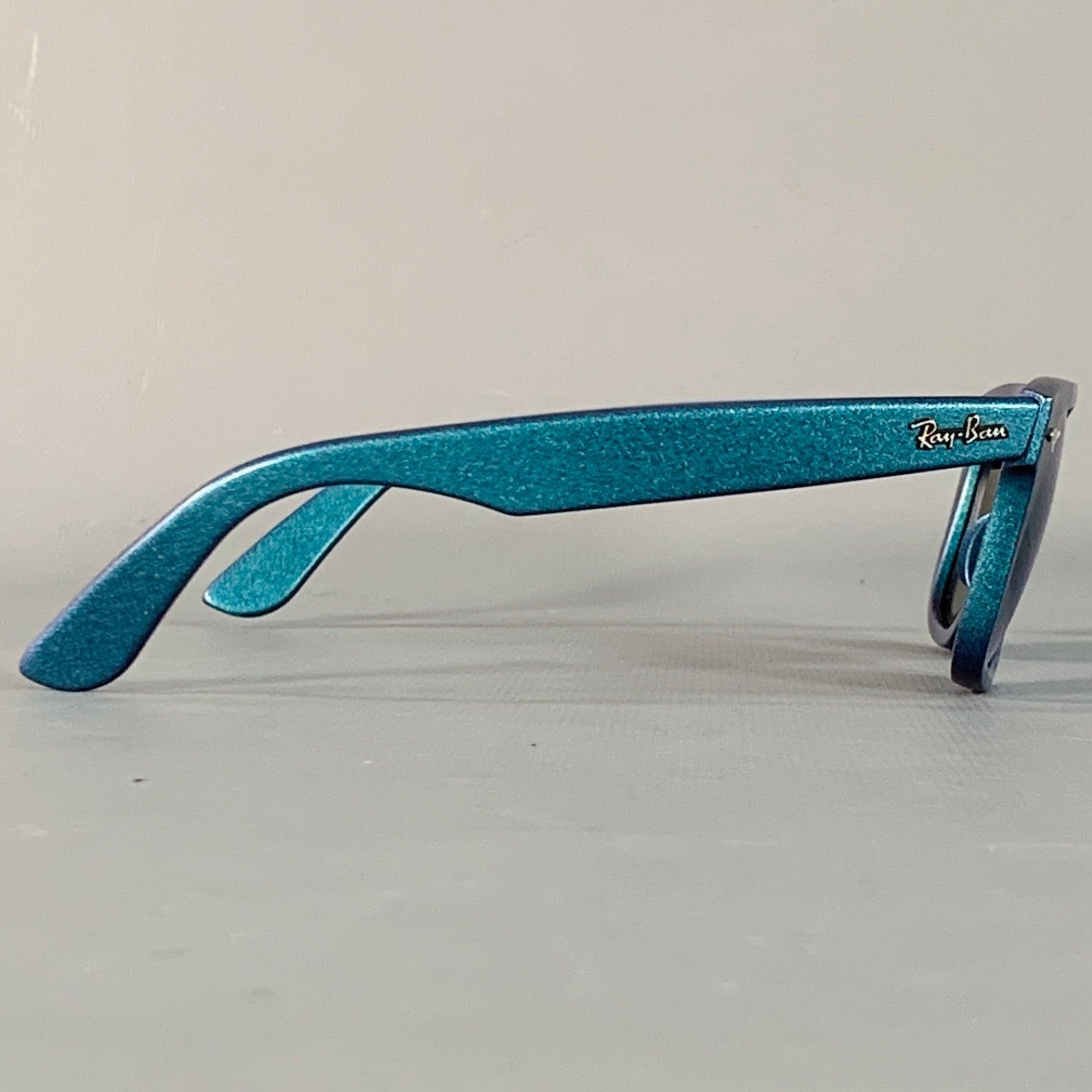 Occhiali da sole Ray-Ban COSMO COLLECTION in acetato glitterato blu con il classico stile Wayfarer e lenti a specchio. Viene fornito con una custodia. Realizzato a mano in Italia. Eccellente condizione di usato. 

Contrassegnato:   RB 2140 

Misure: