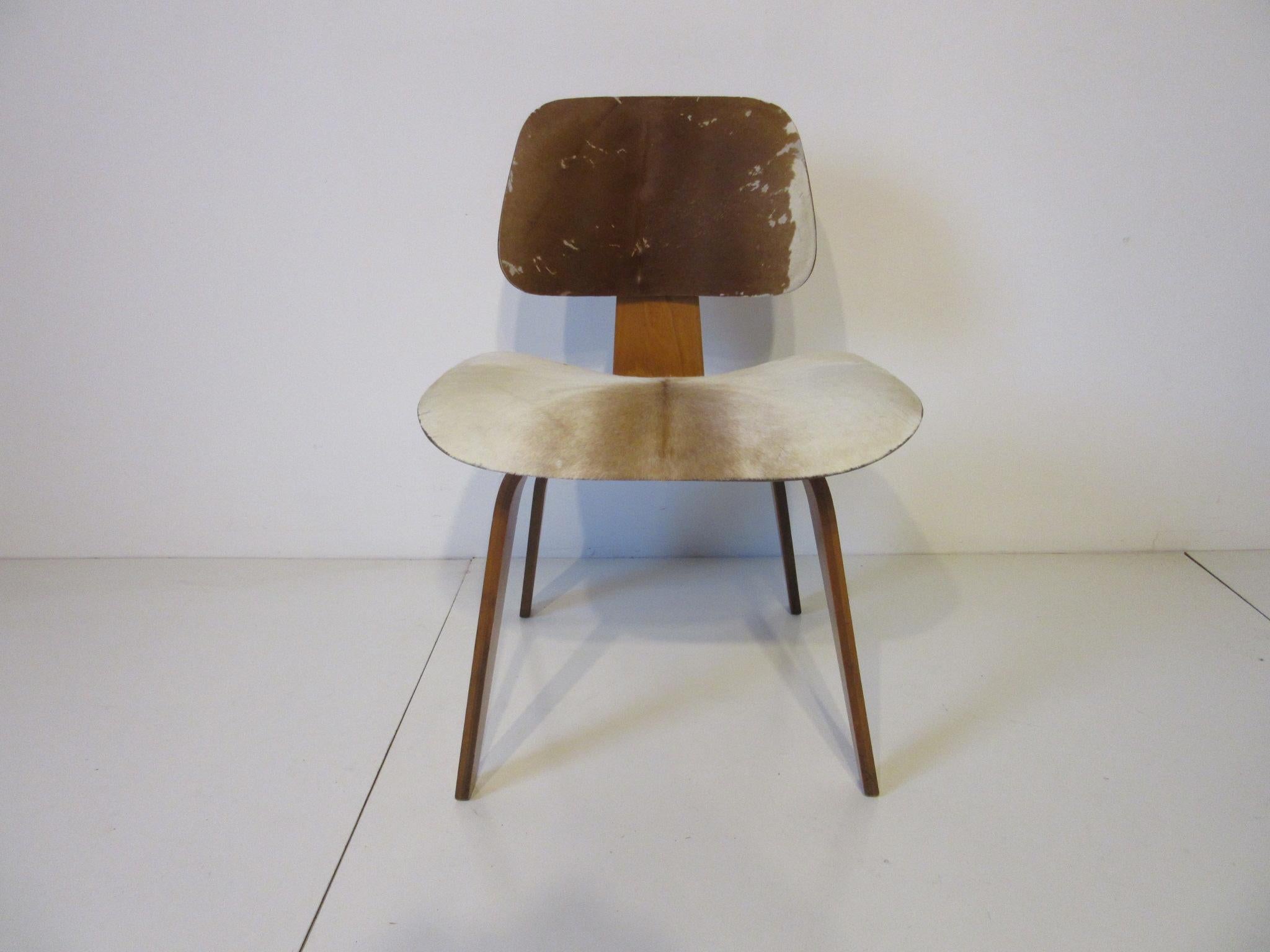 A molded ash plywood DCW (dining chair wood) frame with slunk skin upholstered seat and seat back. Produced between 1948-1953 and having the early 12 screw configuration to the bottom these were a special order item from the manufacture Evans