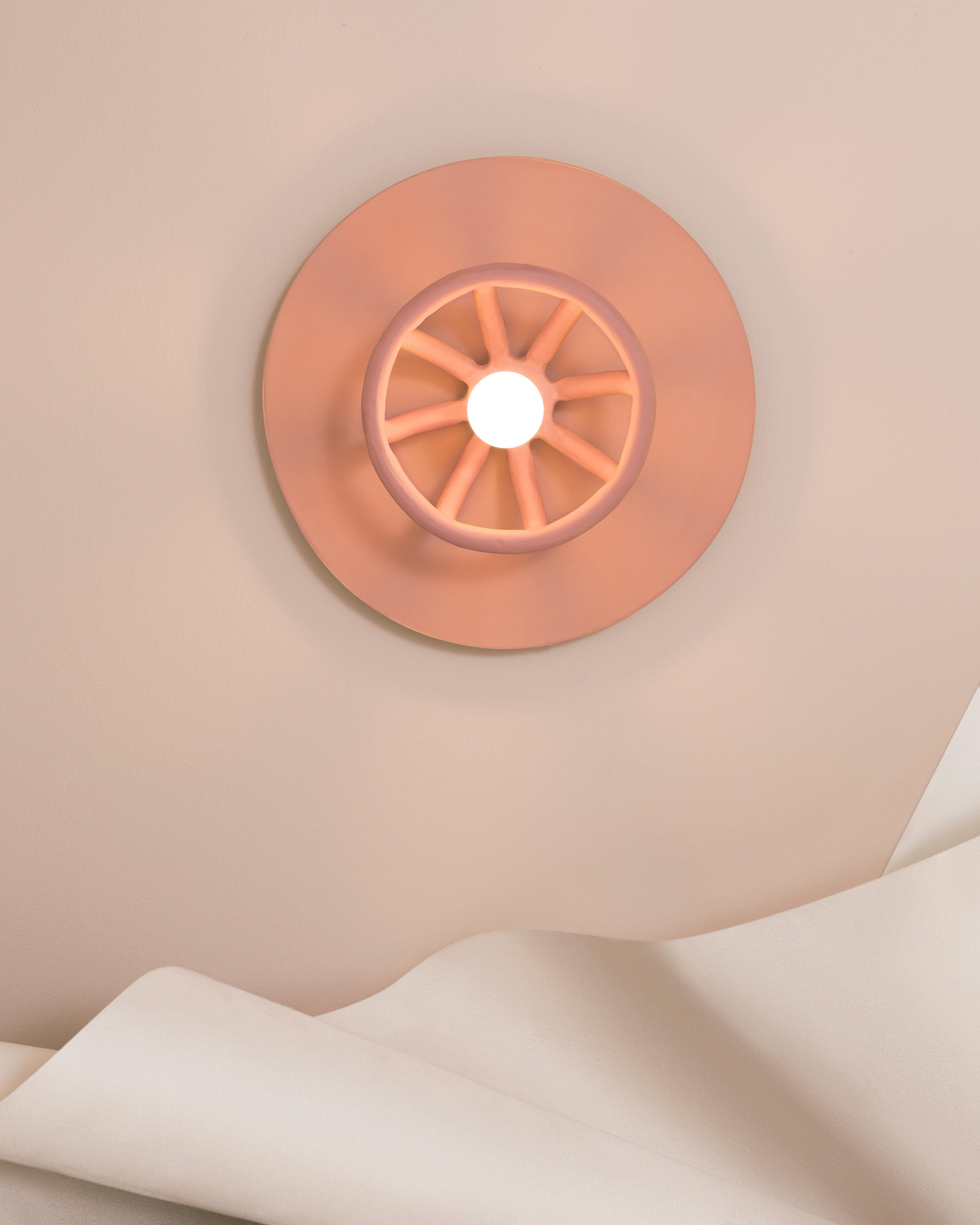 The hand-built ceramic coils cast a dramatic sunburst pattern. The stoneware and terracotta backplate adds warmth, while the glow is punctuated by the exposed light bulb, referencing the rays of light that radiate from the sun.

Material: Speckled