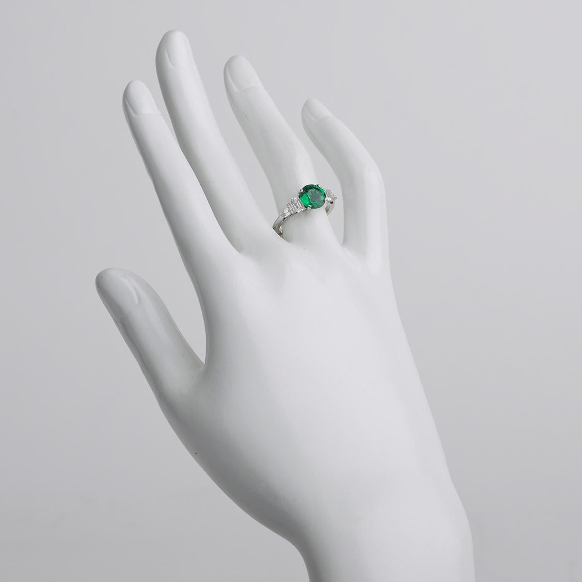 Emerald and diamond ring, centering a round faceted emerald weighing 1.65 carats flanked by two larger modified baguette-cut diamonds with smaller round and bullet-cut diamond accents, in platinum. Diamonds altogether weighing 0.77 total carats.
