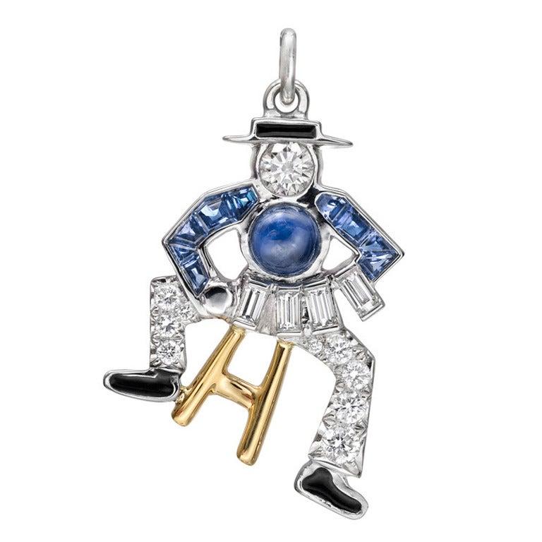 Accordion player gem-set and black enamel charm in platinum on 18k yellow gold stool. Central cabochon-cut sapphire weighing 0.27 carats, nine calibre-cut sapphires weighing 0.14 total carats, larger round brilliant cut diamond weighing 0.08 carats,