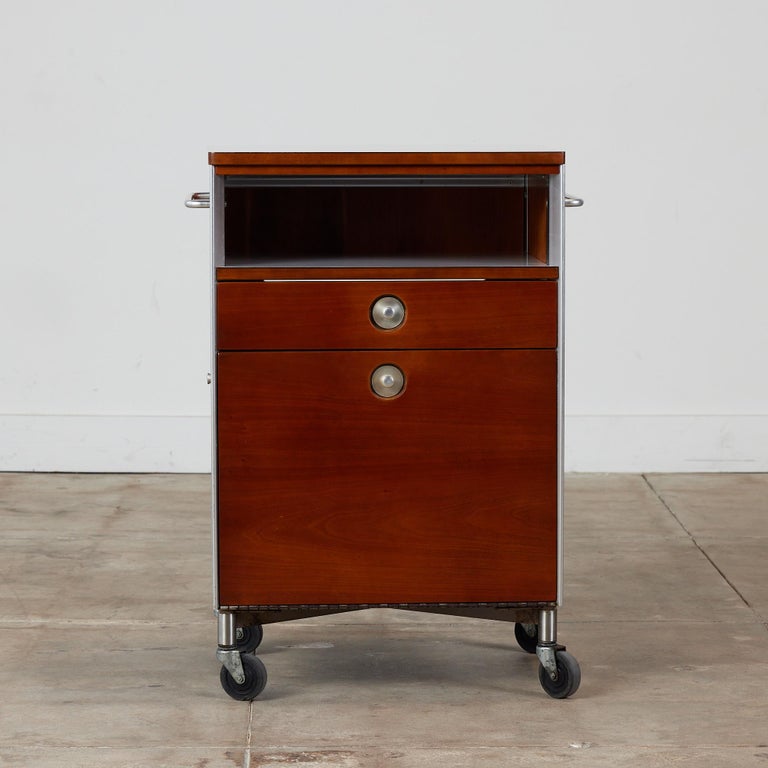 Cherry bar cart by Raymond Loewy for Hill-Rom Company, c.1950s, USA. This industrial design features off white laminate top that resemble a textured linen design. The cabinet has a drawer and door that opens downwards with round aluminum pulls. Each