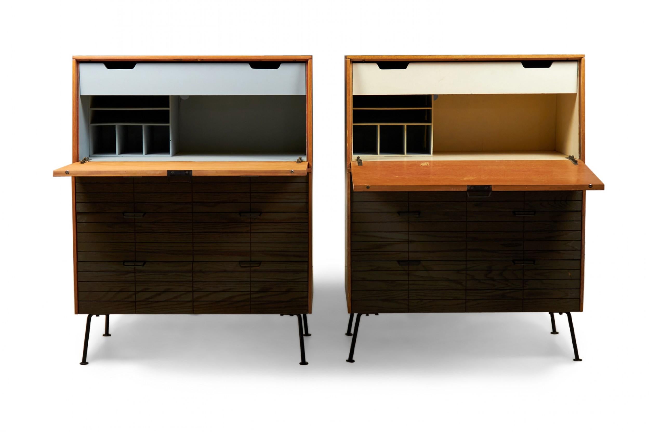 2 American mid-century fall front secretary cabinets with light walnut cases and a front doors that open to create a desk surface and reveal a light gray or beige painted interior with various storage compartments above a 6-drawer cabinet bottom