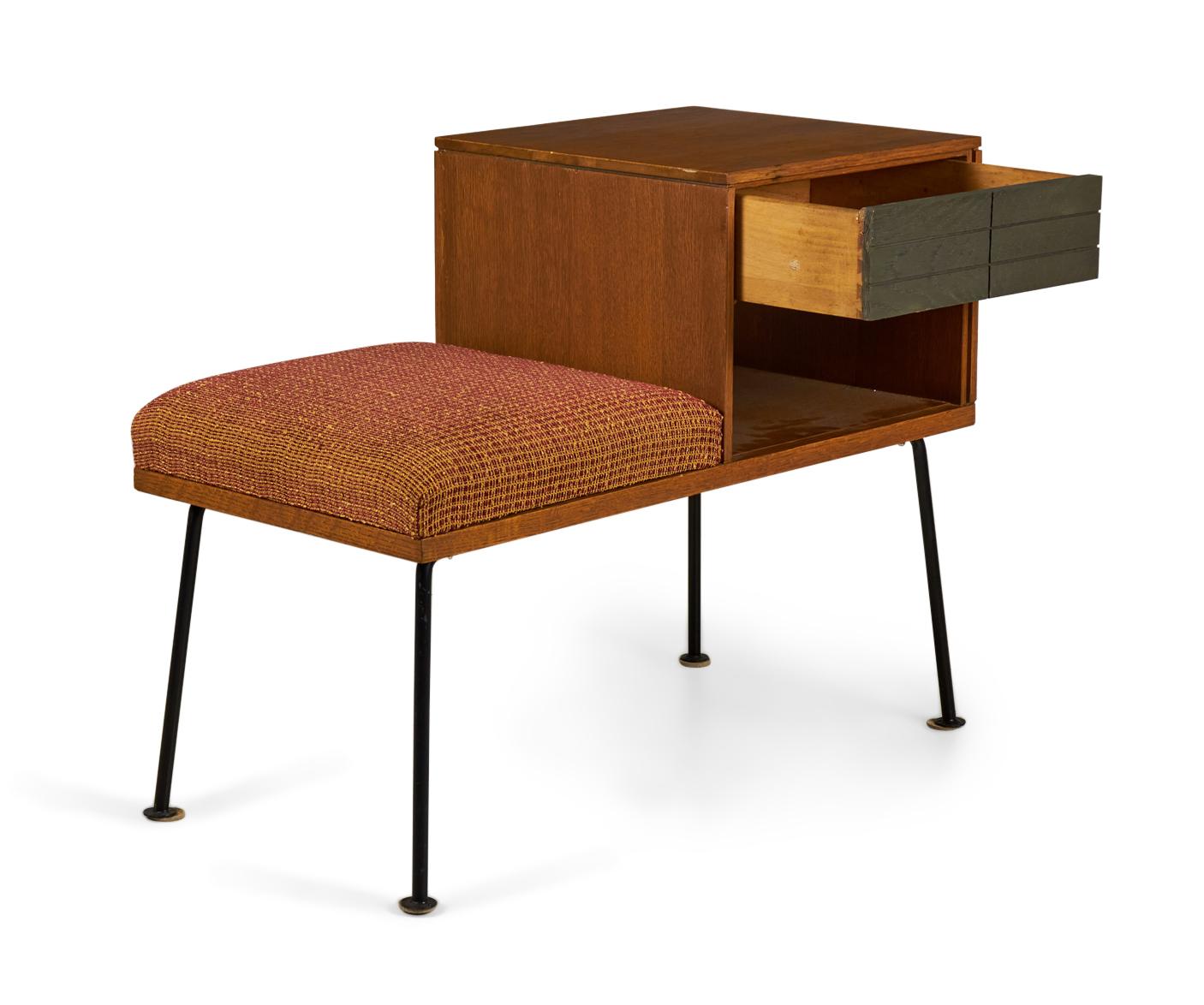 American Mid-Century walnut telephone bench with a rust orange and maroon textured fabric upholstered seat next to a side table section with a single dark stained, geometrically incised drawer above an open compartment, resting on four angled iron