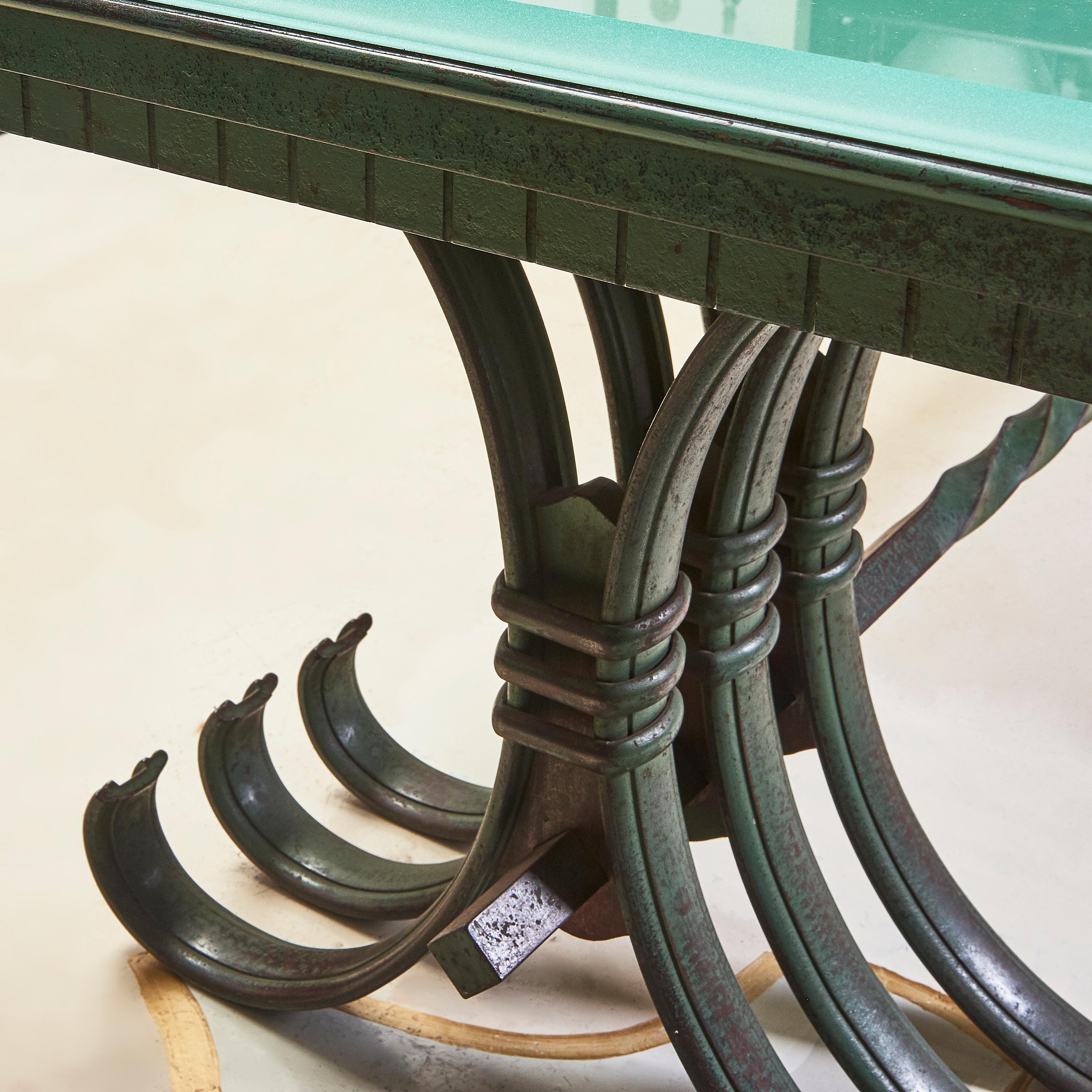 A large French Art Deco style wrought iron dining table, the top with original frosted glass and a bevelled edge. Each of the four c-shaped legs with verdigris patination, conjoined by a central stretcher. In the manner of Raymond Subes, one of the