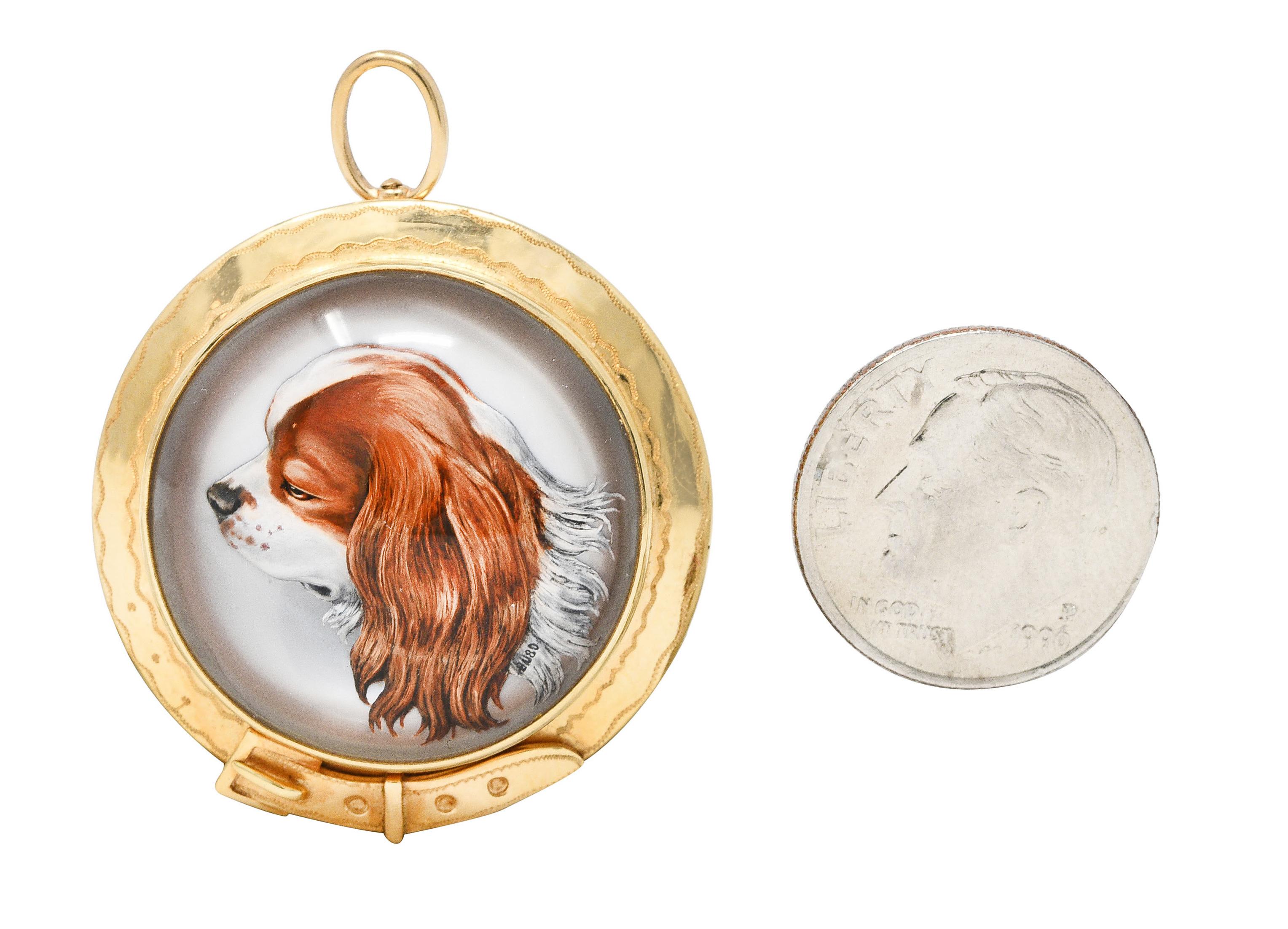 Centering a reverse carved Essex rock crystal cabochon depicting a King Charles spaniel dog. Measuring 23.0 mm round - transparent with opaque white, orange and brown. Backed by mother of pearl - white with subtle iridescence. Bezel set with