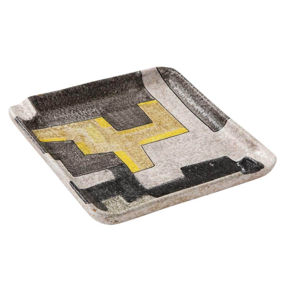 Raymor ashtray, ceramic, geometric, yellow, gray, white, black, signed. Medium scale ashtray, decorated with geometric puzzle pieces and glazed in gray, charcoal, yellow, white, and black. Ashtray has two cigarette or cigar rests. Signed: 