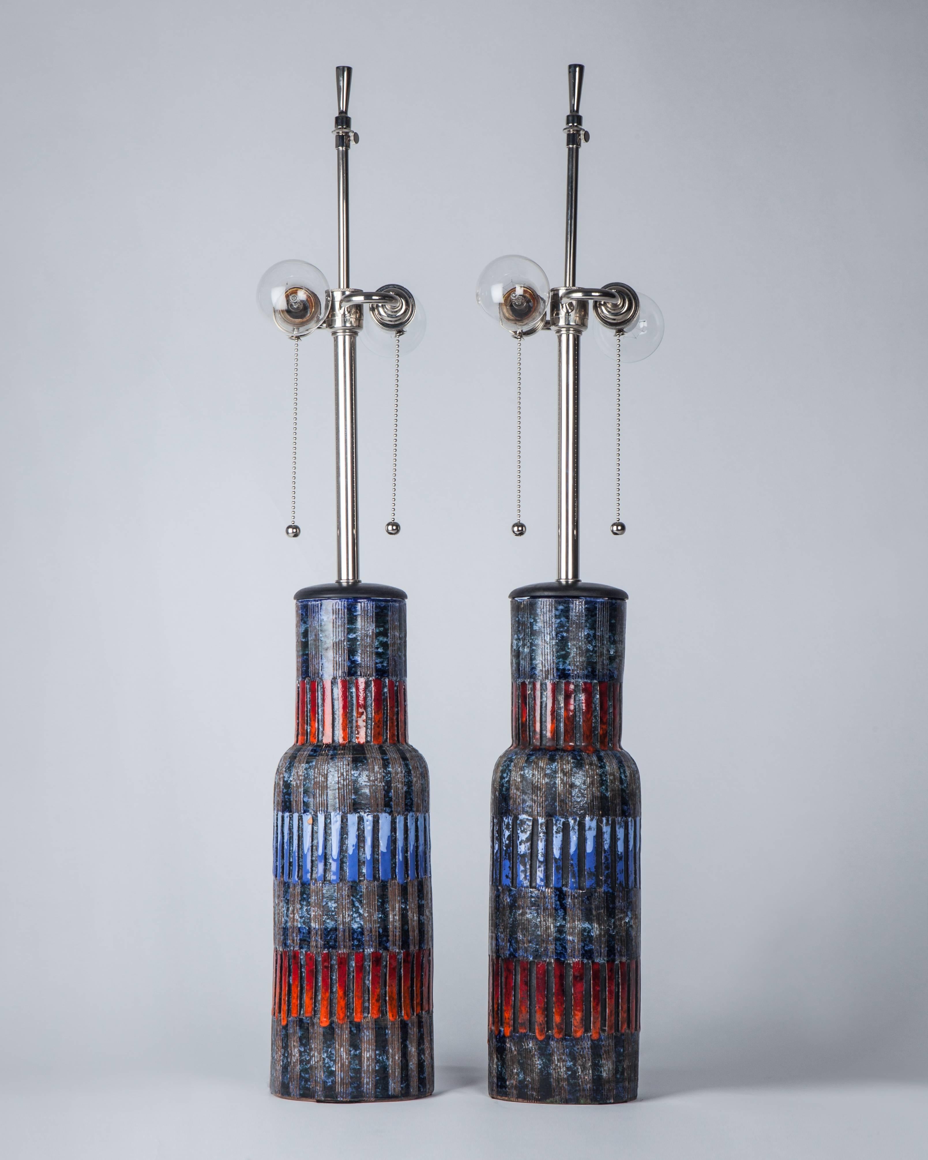A pair of vintage ceramic table lamps with blue, red and charcoal glaze over incised vertical grooves on a shouldered cylindrical form. With dark walnut vase caps and polished nickel fittings. Signed Raymor by Aldo Londi for the Italian maker