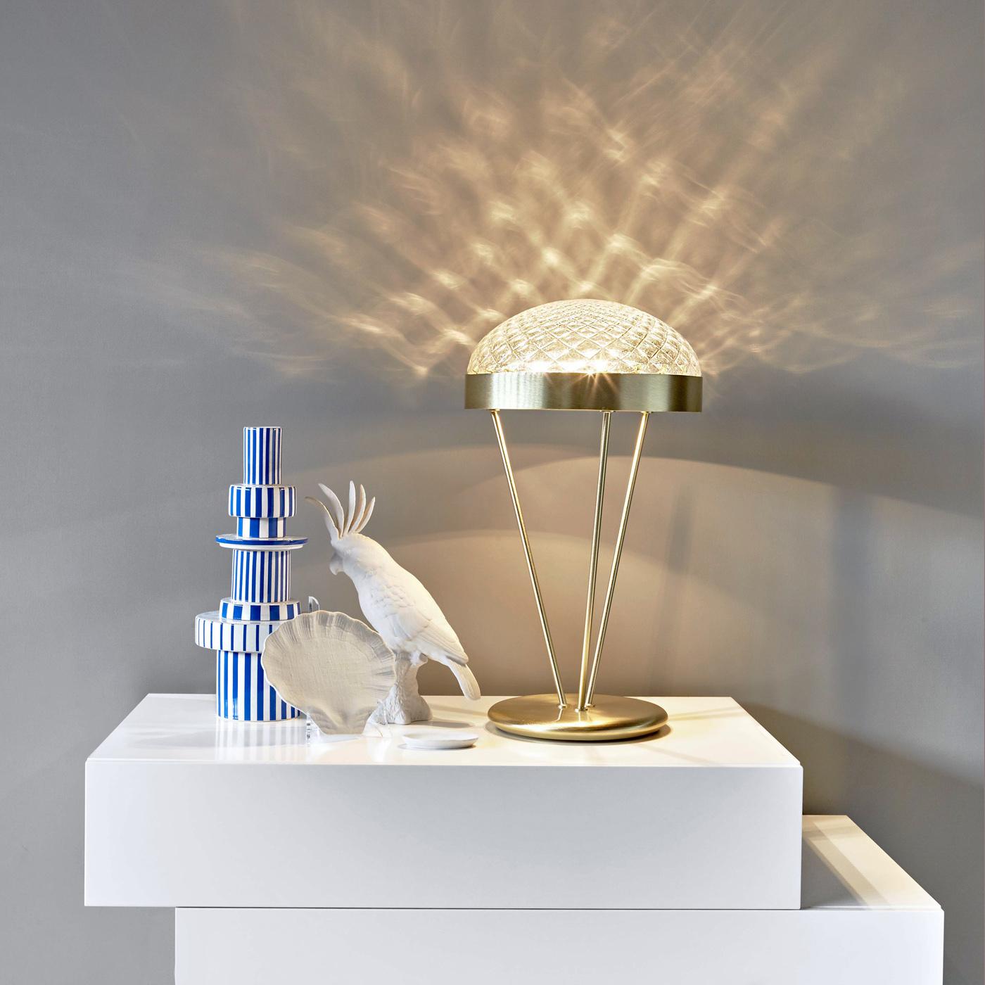 Inspirée des lignes classiques d'une applique, cette élégante lampe de table présente une structure métallique faite à la main avec une finition en laiton poli et un plateau semi-sphérique en précieux verre de Murano. Cette lampe à trois lumières a