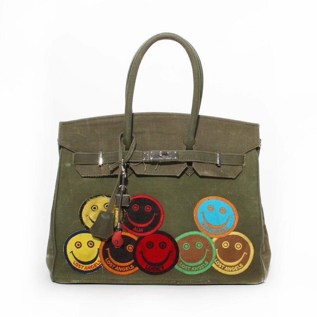 Vintage canvas travel bag by READYMADE
Military green canvas
Dual Top Handle 
Silver-tone hardware 
Smiley patch appliques on front 
Brown canvas interior
Dual slit pockets on interior
Belted turn-lock closure on front flap 
Includes lock, keys and