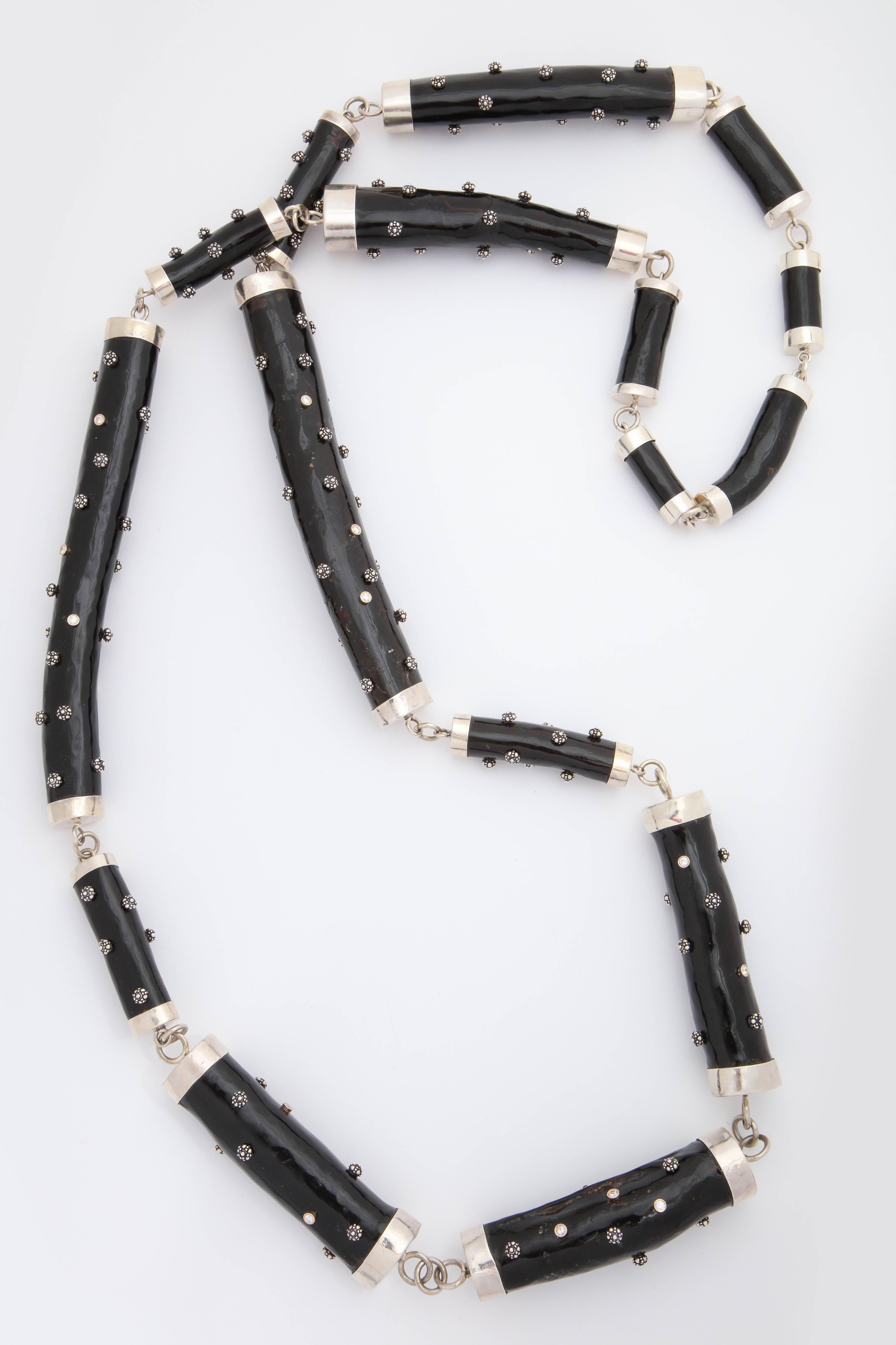 A necklace composed of natural black coral, bezel set diamonds and and sterling silver. The coral branches have sterling silver caps and are linked together with sterling silver rings. The coral is set with sterling silver flowers and bezel set