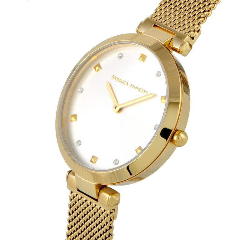 This is the Rebecca Minkoff Nina watch, reference number 2200300. It is presented with a gold ion-plated stainless steel case that is mounted onto a matching gold-tone stainless steel mesh bracelet. The case measures 33 mm in diameter and is