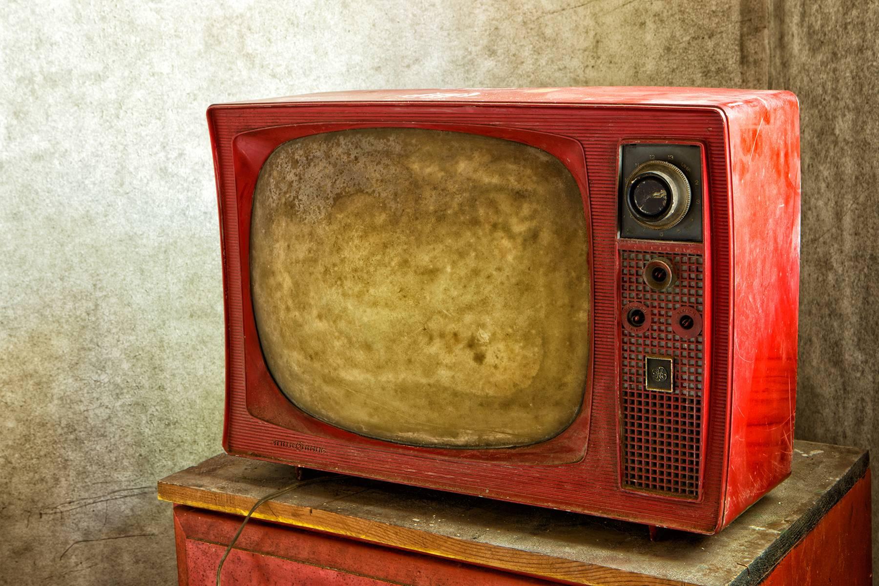 Rebecca Skinner’s “Aged #2” is a 30 x 40 inch metal print and is part of her “Transient” series. The close up color photograph is of a bright red vintage television abandoned long ago. The frameless print has a satin finish is infused directly into