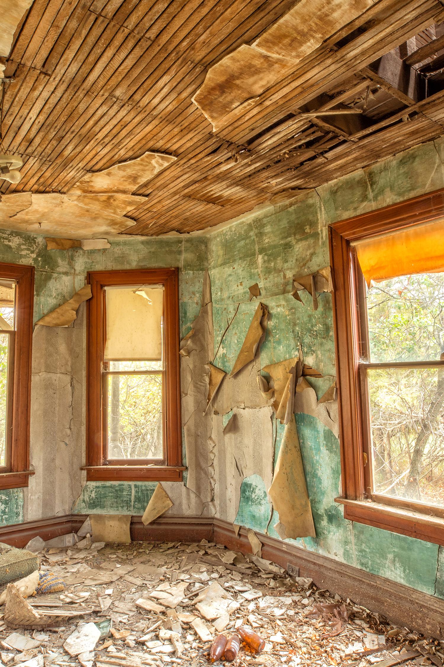 Rebecca Skinner’s “Interior II” is a 12 x 18 inch color photograph taken from inside an abandoned farmhouse in North Dakota. Three windows offer a peak at the surrounding overgrowth in a dilapidated living room with colors of blue, green and brown.