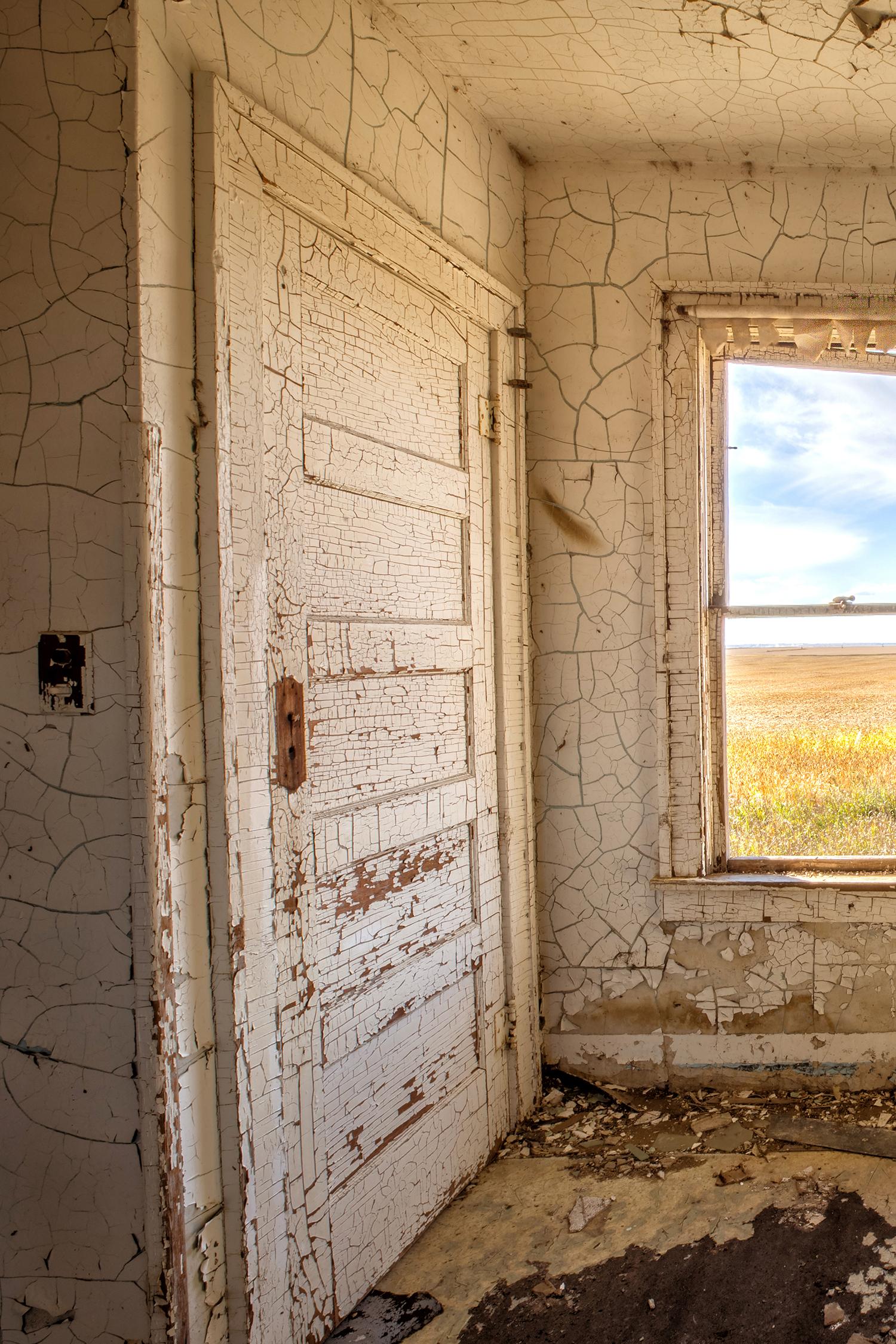 Rebecca Skinner’s “Interior III” is a 12 x 18 inch color photograph taken from inside an abandoned farmhouse in North Dakota. The viewer gets a glimpse of the beautiful landscape thru a dilapidated kitchen window surrounded with walls of white