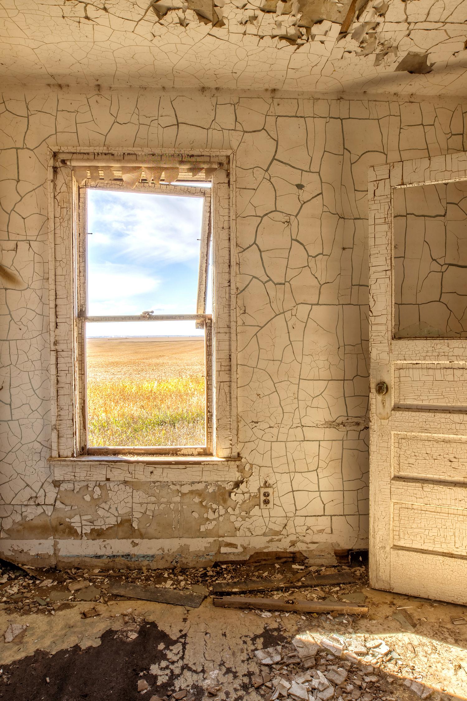 Rebecca Skinner’s “Interior III” is a 12 x 18 inch color photograph taken from inside an abandoned farmhouse in North Dakota. The viewer gets a glimpse of the beautiful landscape thru a dilapidated kitchen window surrounded with walls of white