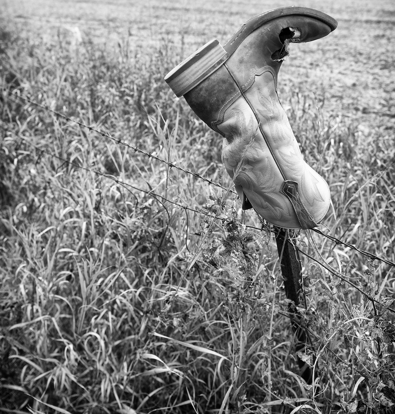 Rebecca Skinner’s “Sorrow” is a 24 x 16 inch contemporary black and white photograph of a weathered cowboy boot resting on a fence in the beautiful North Dakota landscape. The frameless metal print has a satin finish and is infused directly into