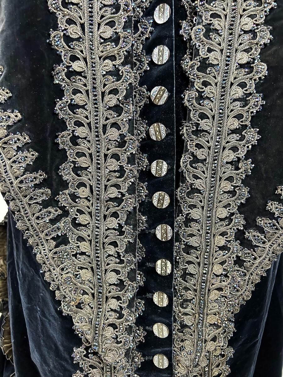 CIRCA 1885-1890 Frankreich
Empfangs- oder Festkleid aus nachtblauem Seidensamt, verziert mit einer Kaskade barocker Friese, die mit Markasitperlen bestickt sind, und schwarzer und goldener Kordelborte. Dieses Kleid in Prinzessinnen-Linie mit