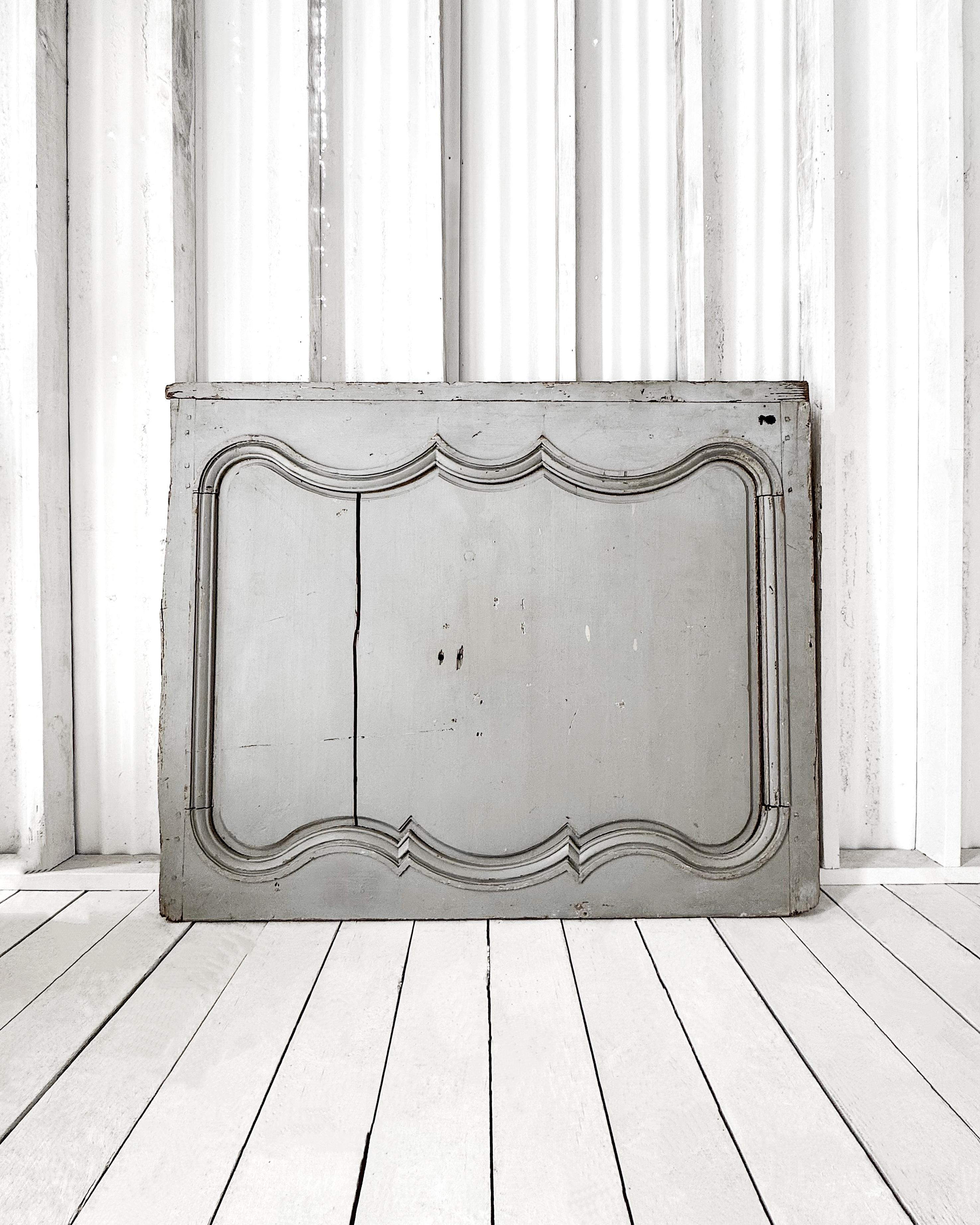 An eye-catching mid-19th-century French boiserie panel retains its original pale French blue paint, gently worn to reveal the wood grain and character beneath.

The panel’s carved molding features symmetrical scrollwork with a double peak at the top