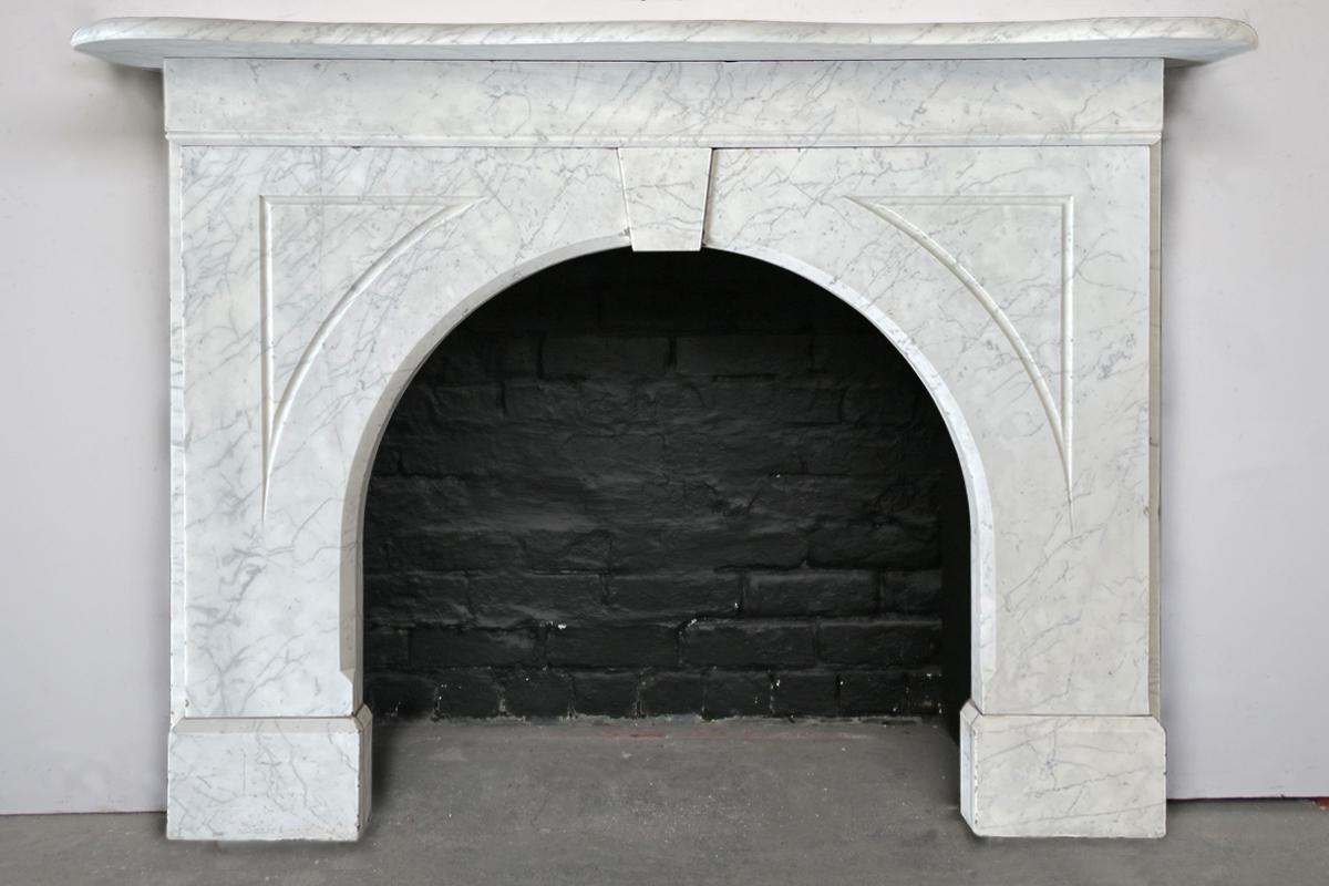 An arched Victorian Carrara marble fireplace surround of good proportions. The plain frieze sits below a serpentine mantle with a bullnose edge and above a plain keystone and flutes to the arched spandrels. Circa 1860.

This surround is currently