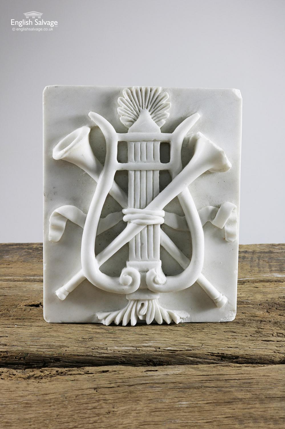 Carved marble rectangular plague with a musical themed design featuring two trumpets tied with ribbon to what looks like an ancient style harp. The depth below is of the rectangular marble back, the overall depth is 4.5cm. One of the trumpets has a