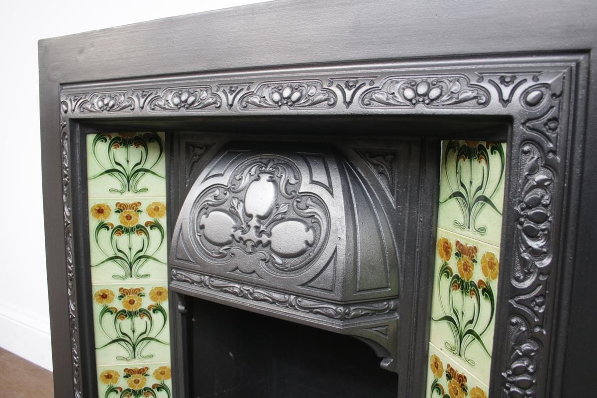 Reclaimed Edwardian Art Nouveau tiled fireplace grate, circa 1905. Complete with an original set of antique fireplace tiles.
The cast iron has been finished with traditional black grate polish and is supplied with a new replacement clay fireback