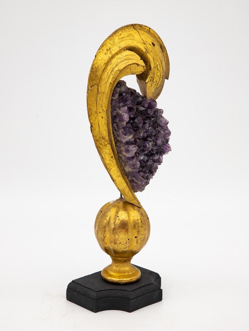 A reclaimed giltwood fragment on a stand. This reclamation art piece is finished with an amethyst at the crown. A lovely combination between the bright gold and the soft amethyst color, this one-of-a-kind piece was discovered in France.