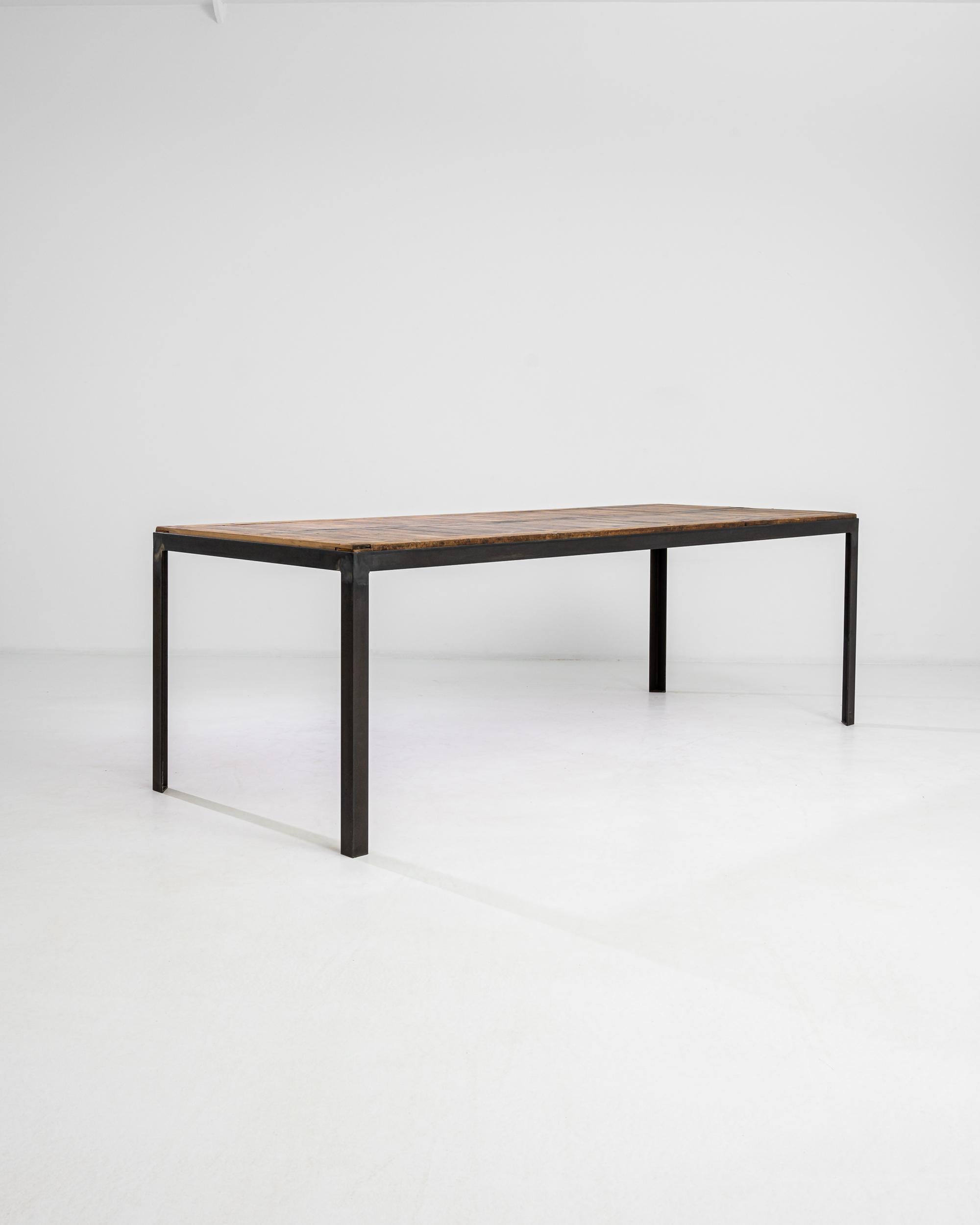 Composed with 20th century architectural salvage from France, this table boasts an industrial steel frame that elevates a wooden table top. The texture and color of the wooden surface enhance the minimal aesthetic of the black-patinated metal base.