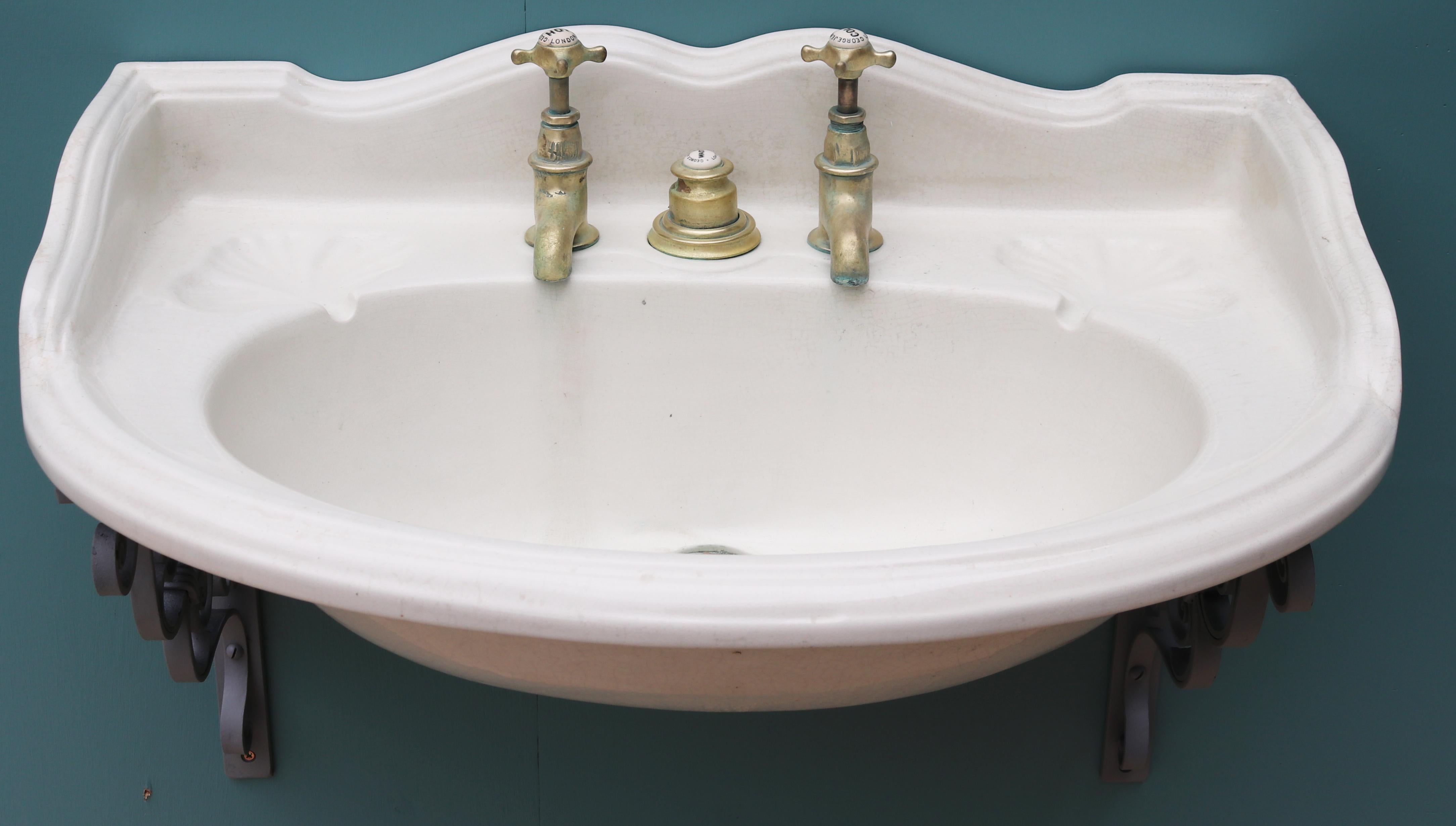 A rare George Jennings wash basin, made from porcelain, with brass taps and plunger waste. Wall mounted with wrought iron brackets. Good structural condition. Original plunger waste system present. Original taps present. These move freely, but are