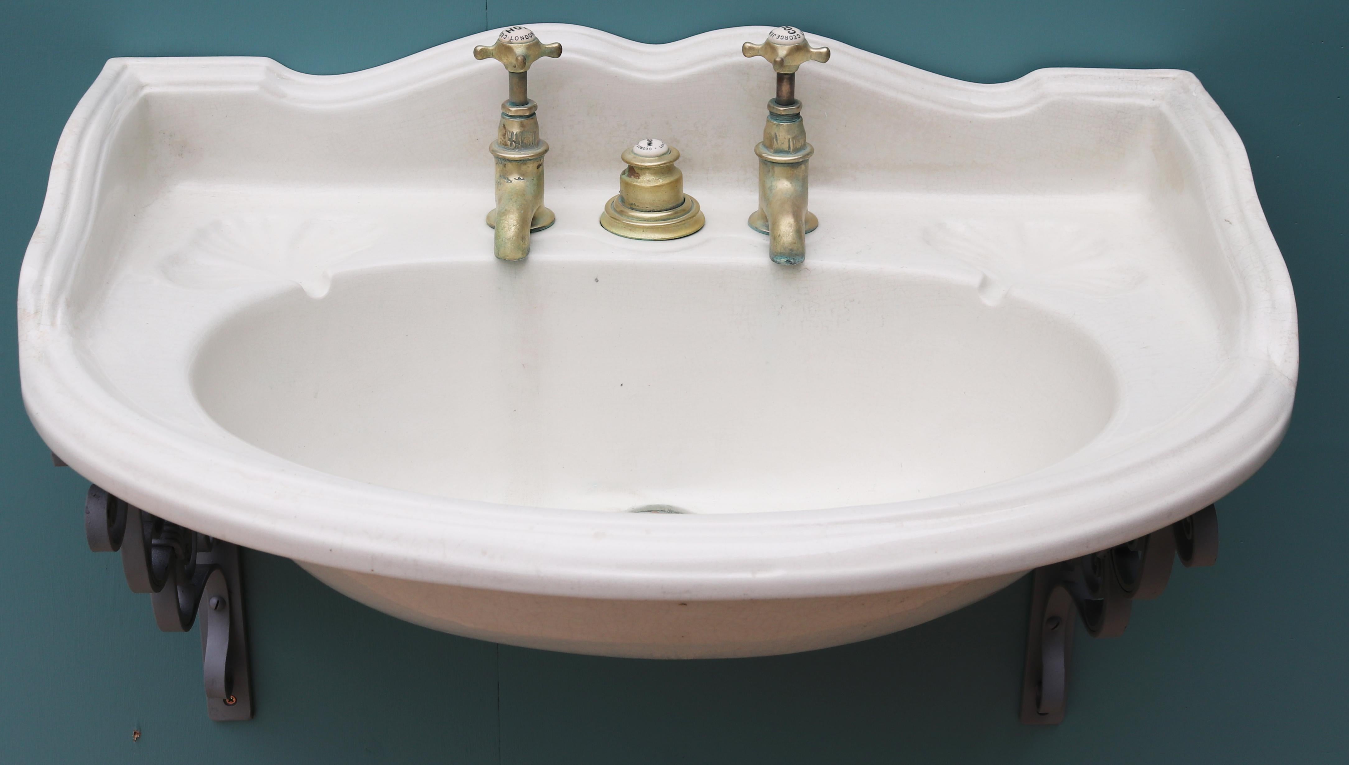 Ein seltenes George-Jennings-Waschbecken aus Porzellan, mit Messingarmaturen und Kolbenabfluss. Wandmontage mit schmiedeeisernen Halterungen. Guter baulicher Zustand. Original-Kolbenabfallsystem vorhanden. Original Wasserhähne vorhanden. Diese sind