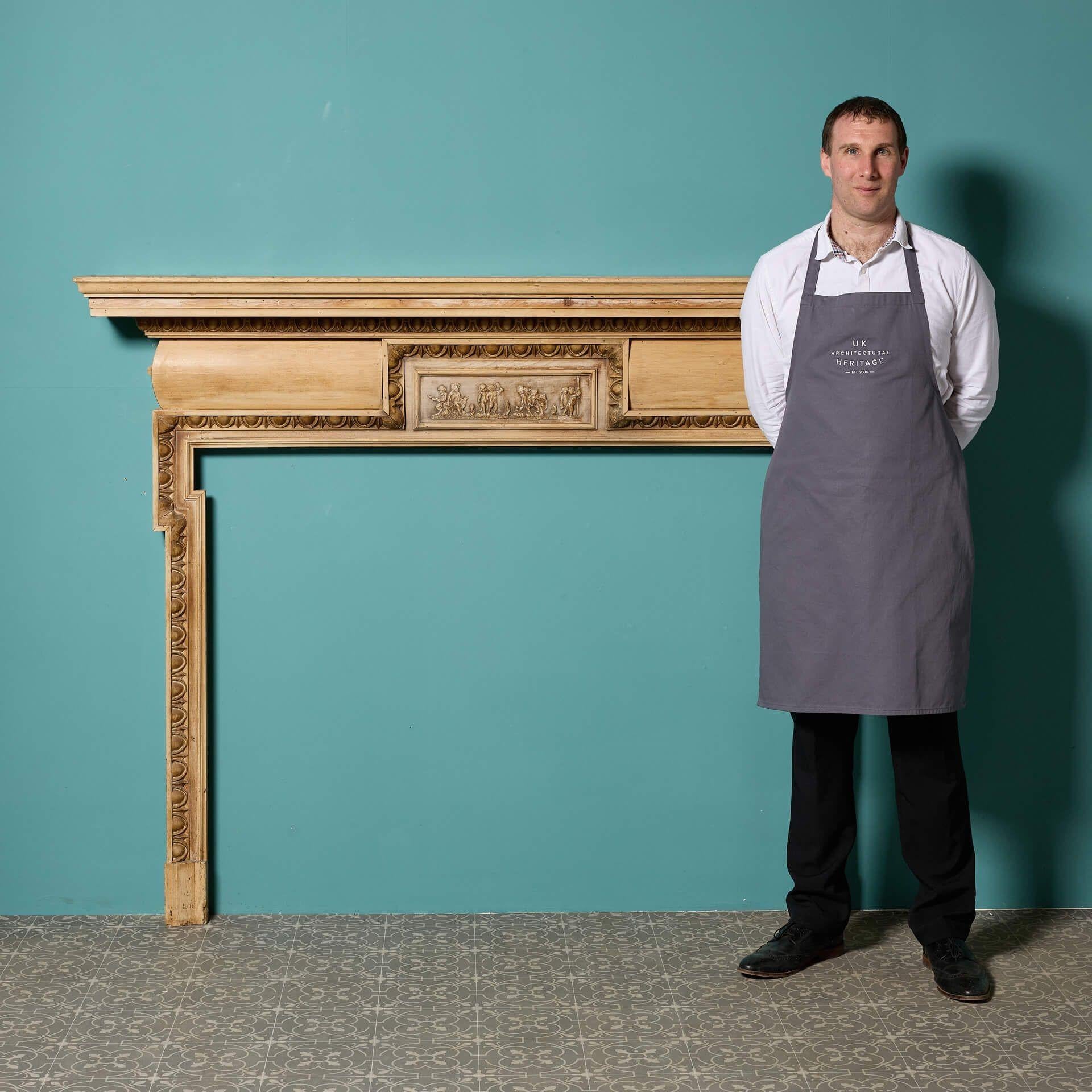 A large reclaimed Georgian style pine and composition fire surround, circa 1870. This striking pine fireplace is typical of Georgian styling with its egg and dart edged dog leg opening and central frieze tablet depicting composition putti.

