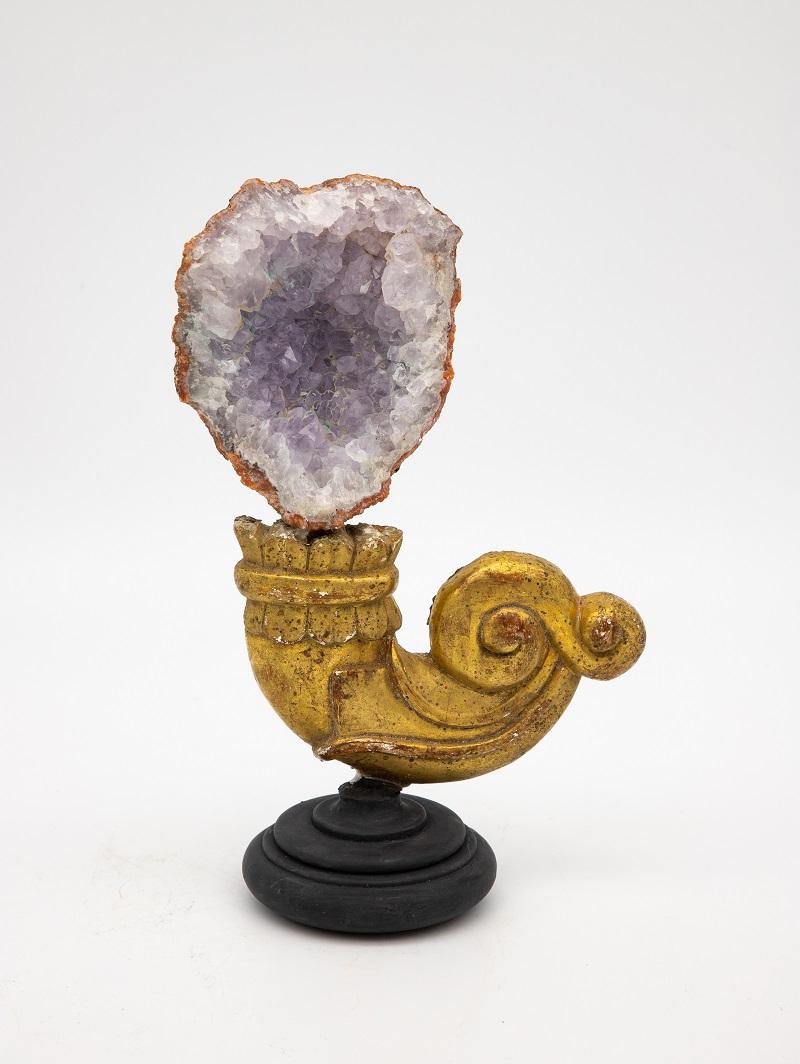 A reclaimed giltwood fragment on a stand. This reclamation art piece is finished with an amethyst at the crown. A lovely combination between the bright gold and the soft amethyst color, this one-of-a-kind piece was discovered in France.
