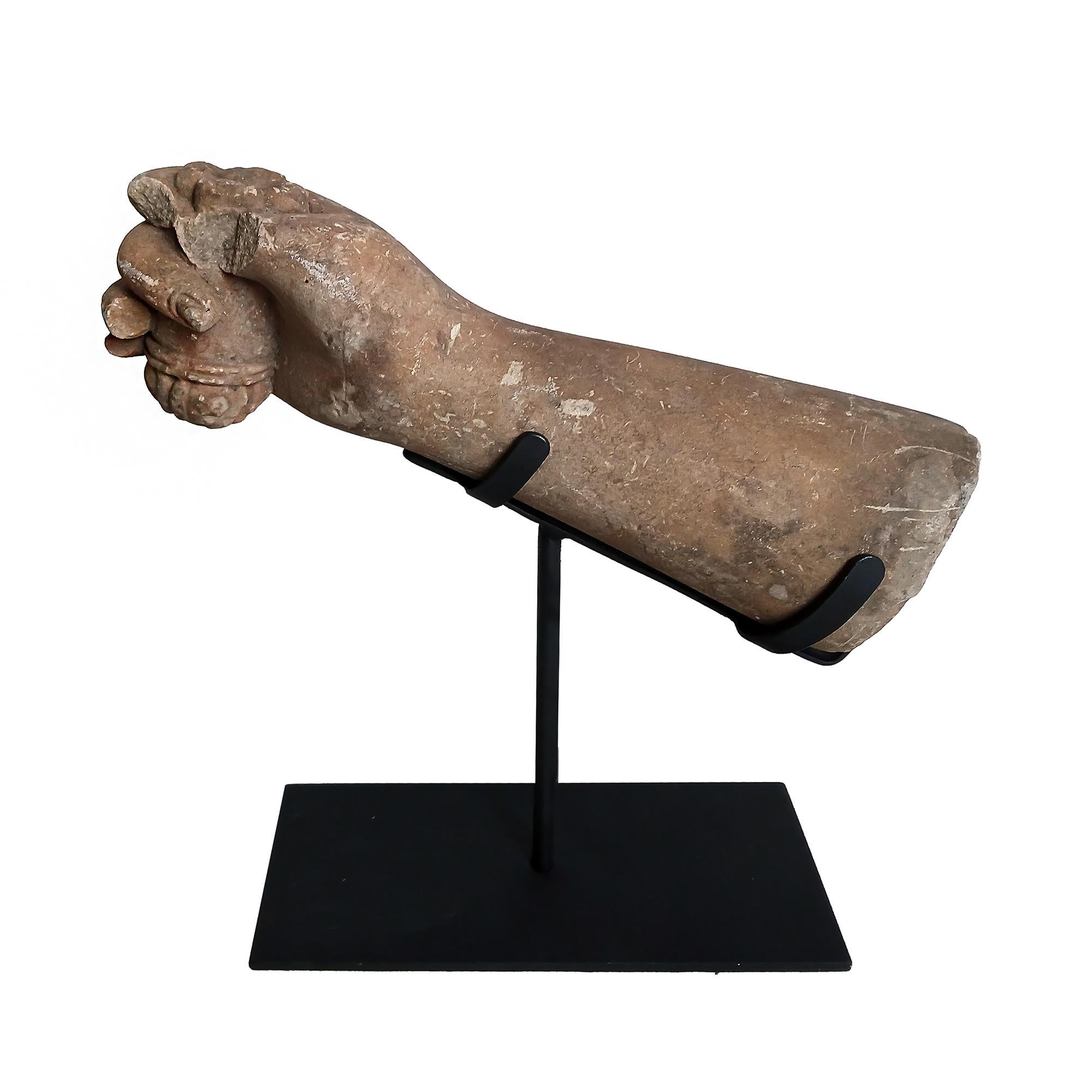 Un frammento di mano che regge un rotolo, recuperato da una statua in pietra Khmer. Thailandia orientale, inizio del XX secolo. 

Scolpito a mano in pietra arenaria marrone/ocra, il frammento faceva parte di una scultura da giardino di una divinità