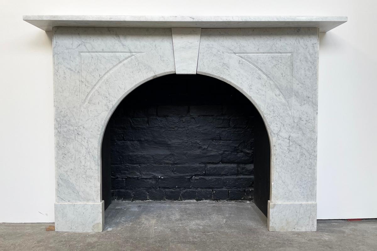 An arched Victorian fireplace surround of good proportions Carrara marble. The simple form benefits from a chamfered inside edge fluting to the spandrels below the square edged shelf flanking an unadorned keystone. Circa 1860.

For detailed sizes