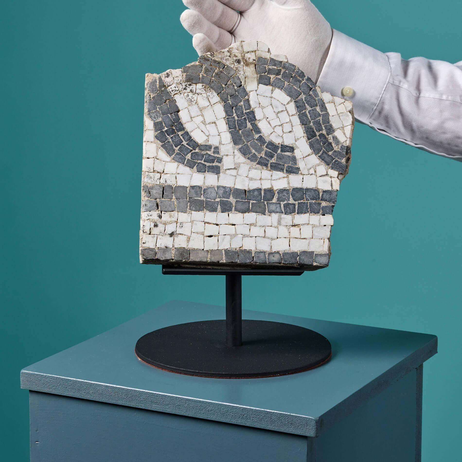 Dieses Mosaik im römischen Stil auf einem Ständer ist ein Fragment der Geschichte. Sie enthält komplizierte Mosaikarbeiten aus kontrastierendem farbigem Marmor, die ihr das Aussehen einer antiken römischen Villa oder eines Badehauses verleihen. Er