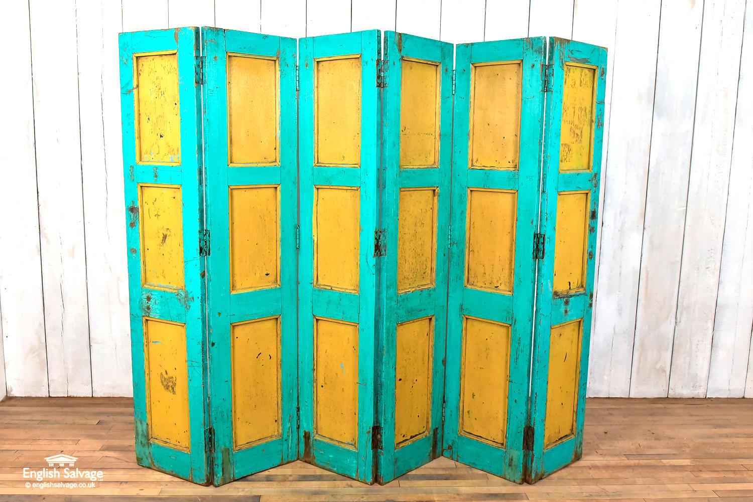 Reclaimed wood panelling in a vibrant teal and yellow color. The reverse is solid turquoise in color. The paint has a weathered patina with some age-related wear and scrapes. The screen is made up of six individual hinged panels (each with a width