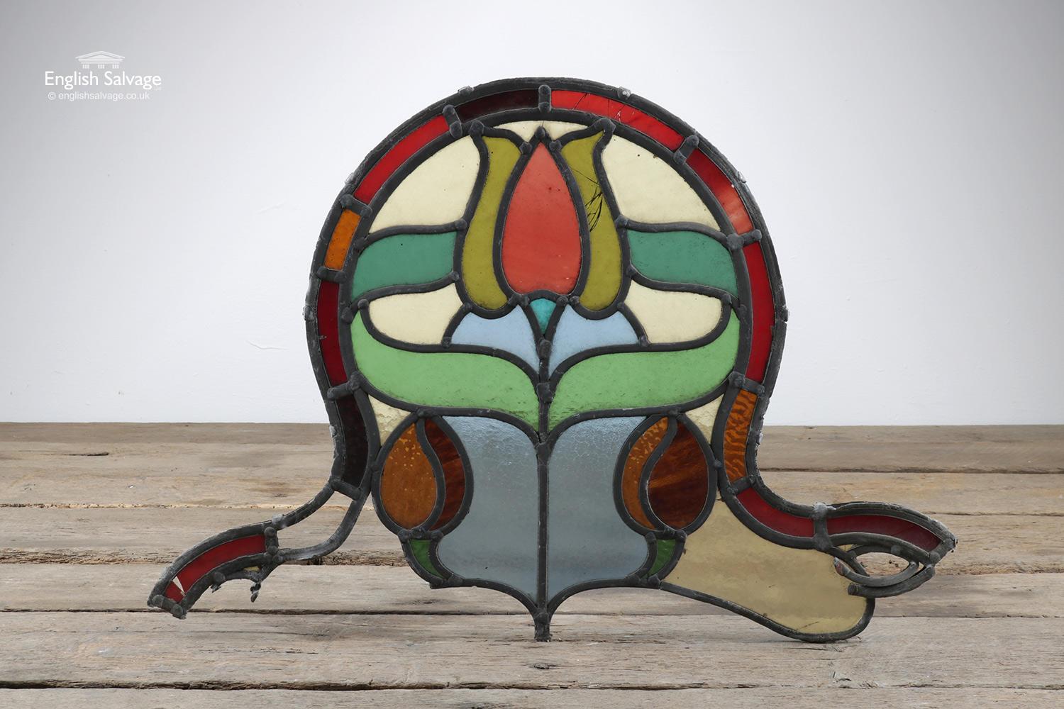 Reclaimed arched stain glass panel depicting a central flower and leaves with a red frame. Cracks to a few glass panes and loss to the bottom of the panel.