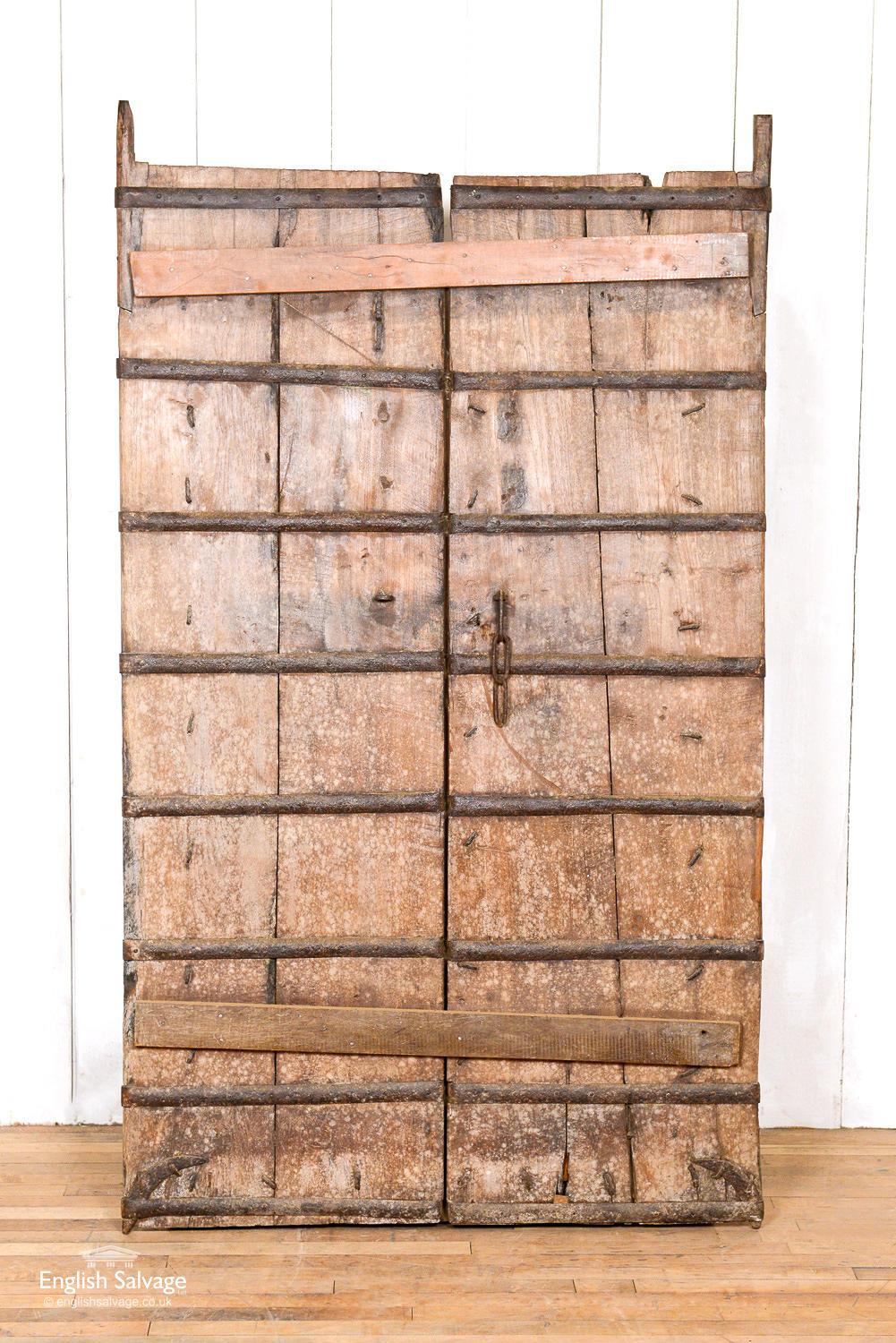 Salvaged teak Indian pair of doors with barred back. Old iron work studs still present. One side with carvings and one side plain. Some scrapes, splits and scuffs commensurate with age.