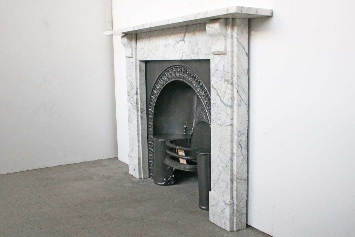 Reclaimed Victorian fireplace surround in well figured Carrara marble with simple geometric corbels supporting the shelf, circa 1870.

Pictured with an original early 19th century cast iron grate, priced separately.

For detailed sizes please