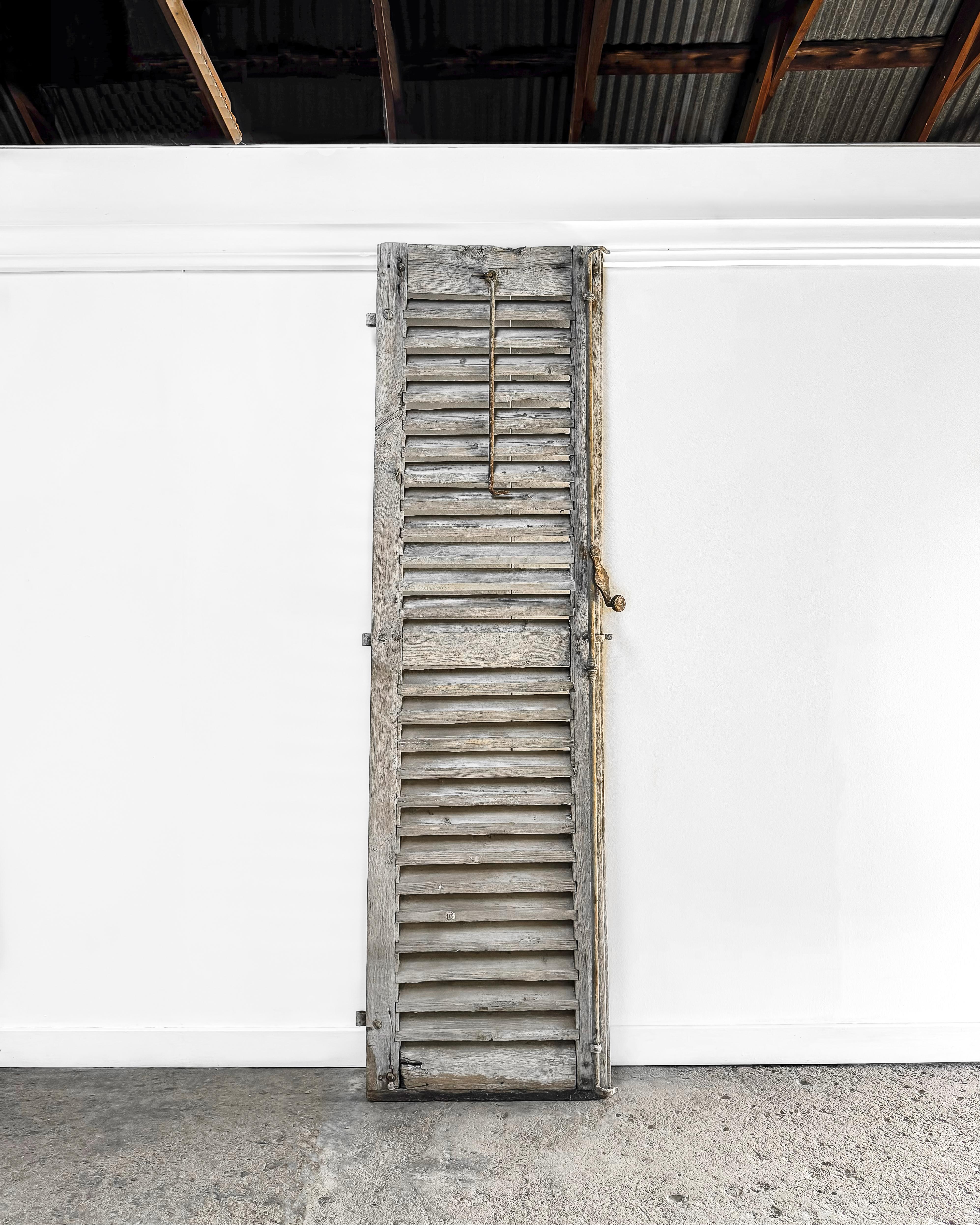 This salvaged, weathered white shutter, adorned with its original iron hardware, is rich in character and brimming with visual appeal. Attach it to sliding barn door hardware for a unique, functional cabinet door, or hang it on a wall as a stunning
