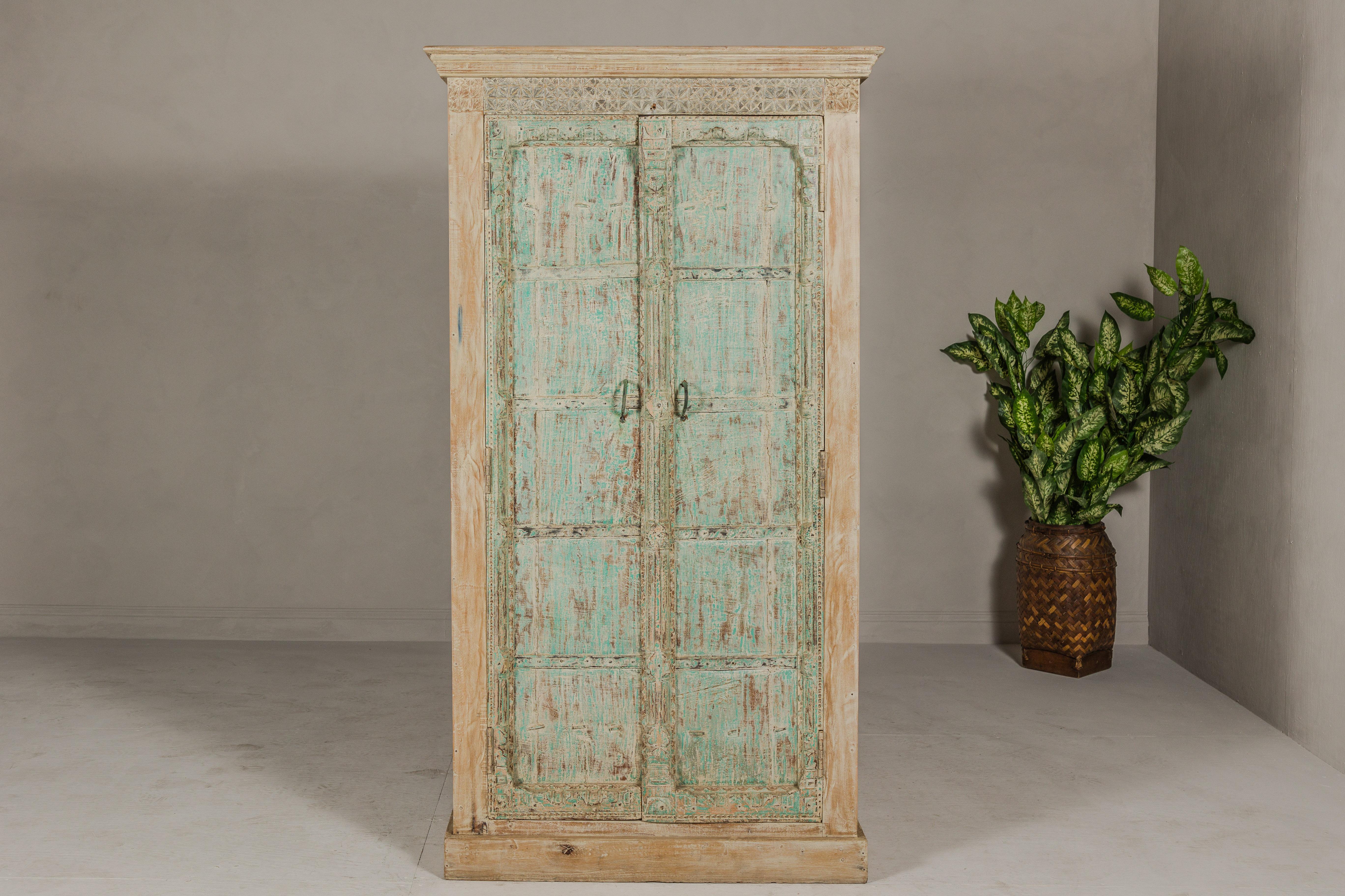 An Almirah armoire made from reclaimed wood, with weathered green patina, three interior shelves and carved décor. Experience the charm and history embedded in this exquisite Almirah armoire, meticulously crafted from reclaimed wood and adorned with