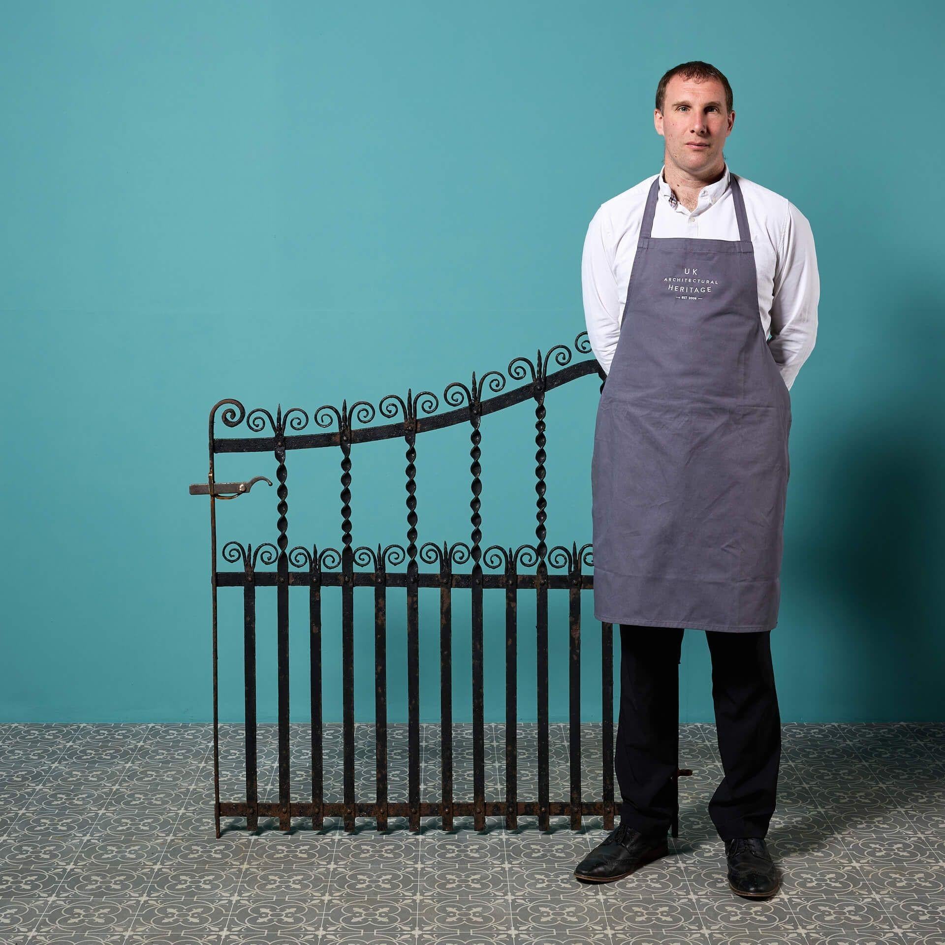 Un cancello pedonale in ferro battuto realizzato da un fabbro, recuperato da una casa di Birmingham. Con il suo arco dolcemente ampio, i binari attorcigliati e le decorazioni a volute, questo cancello laterale antico è un'aggiunta senza tempo ai