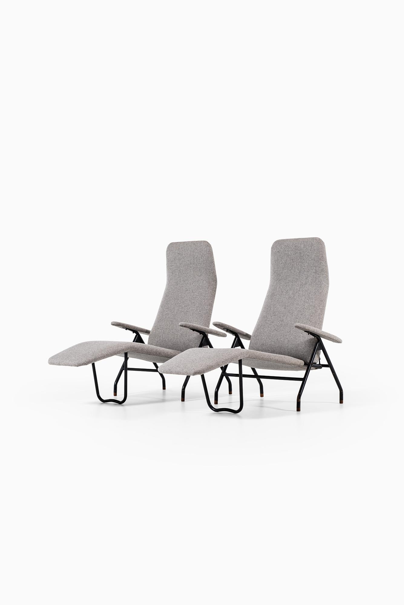 A pair of reclining easy chairs. Produced in Denmark. Black lacquered steel and newly reupholstered in grey fabric.