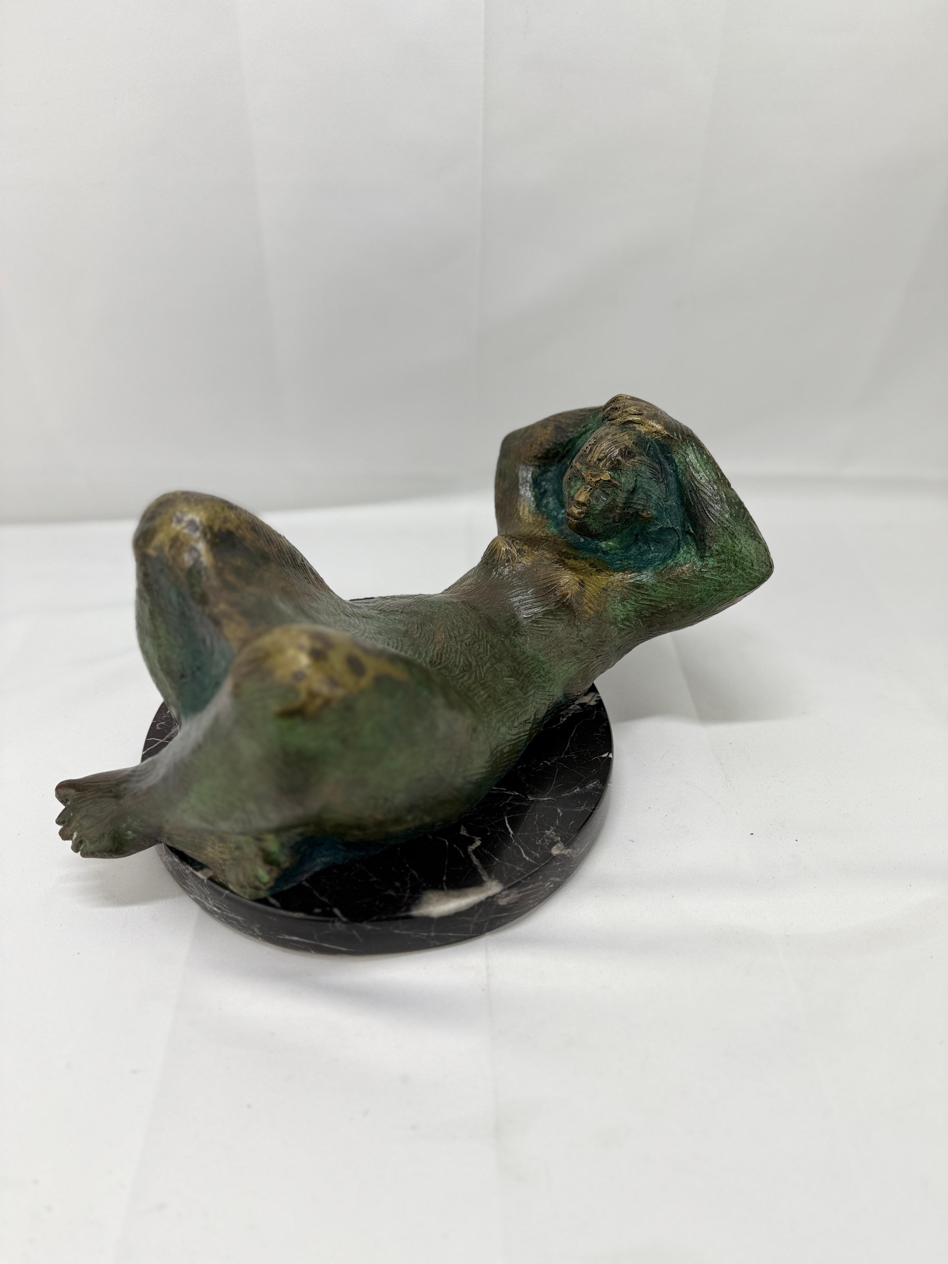 Questa affascinante scultura in bronzo, firmata D. A. 71, raffigura una figura femminile reclinata in una posa serena e contemplativa. La maestria dell'artista è evidente nei dettagli del corpo della figura, che cattura sia il movimento che