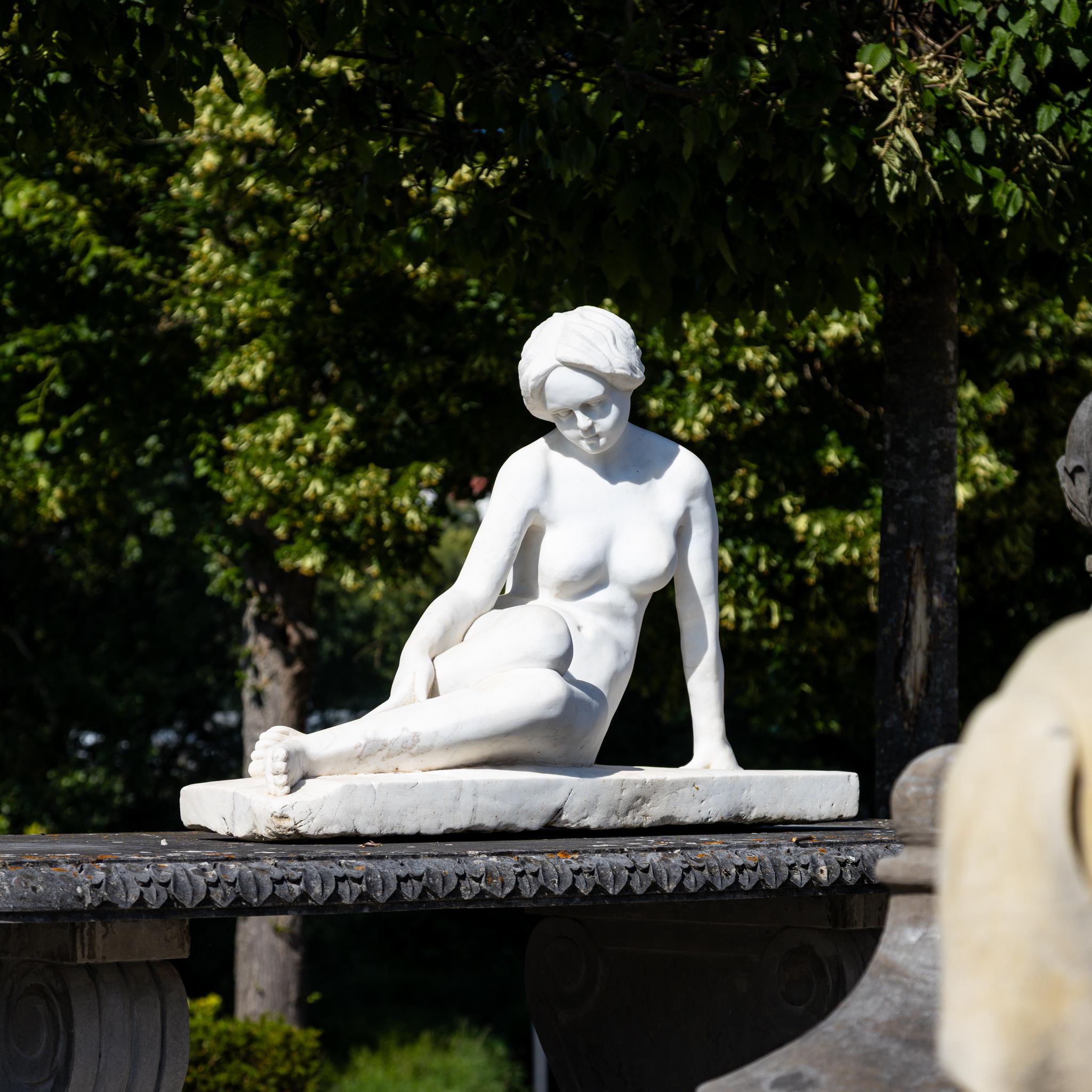 Scultura in marmo di un nudo femminile reclinato. La figura ritrae una donna contemplativa in una posa classica e rilassata, con proporzioni naturali e dettagli finemente scolpiti.
