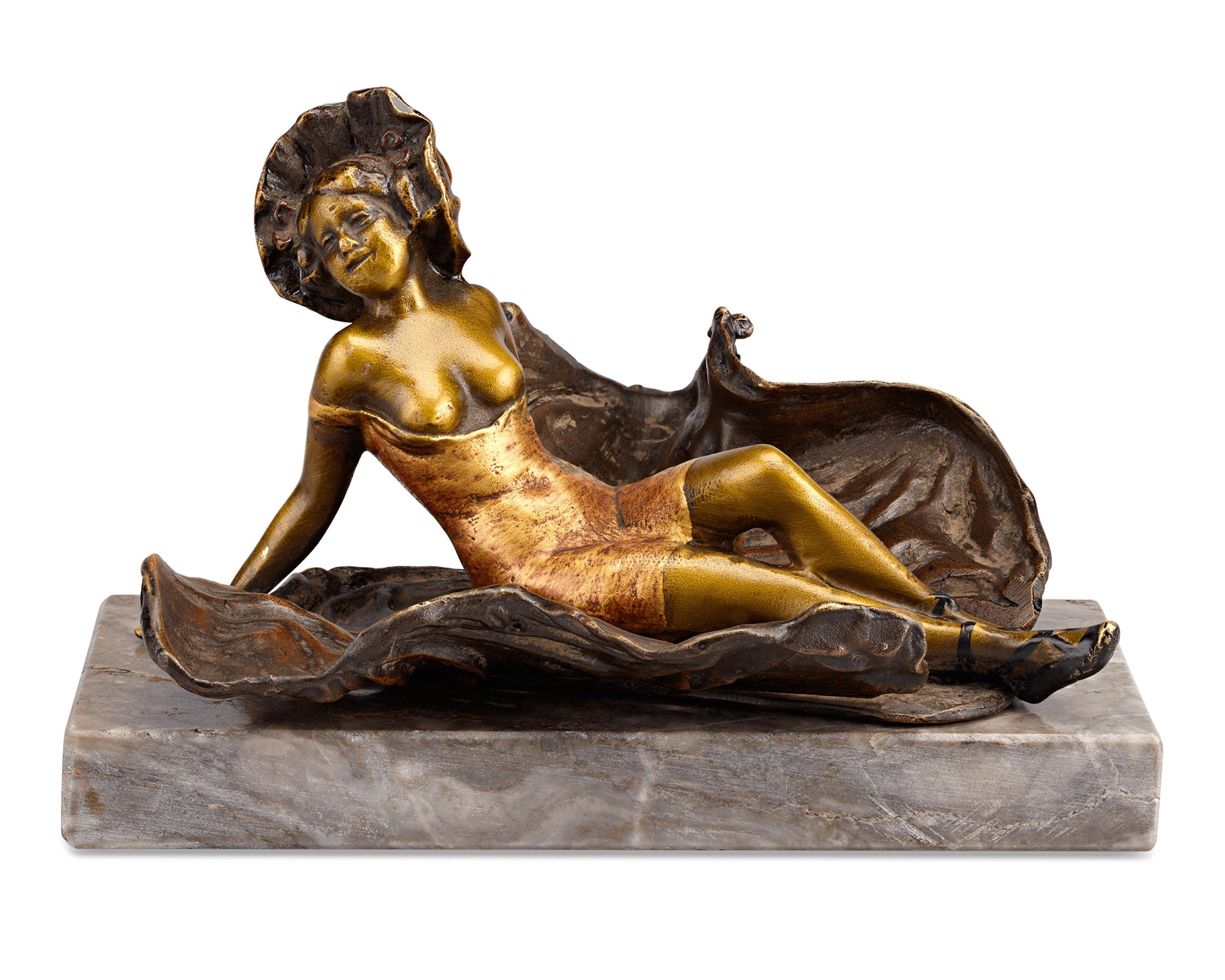 Hinter dieser bezaubernden Belle-Époque-Figur verbirgt sich mehr, als man auf den ersten Blick sieht. Die aus Bronze gefertigte und mit Kaltpressemail versehene Figur einer jungen Frau in ihrem Gewand birgt eine verlockende Überraschung. Dank eines